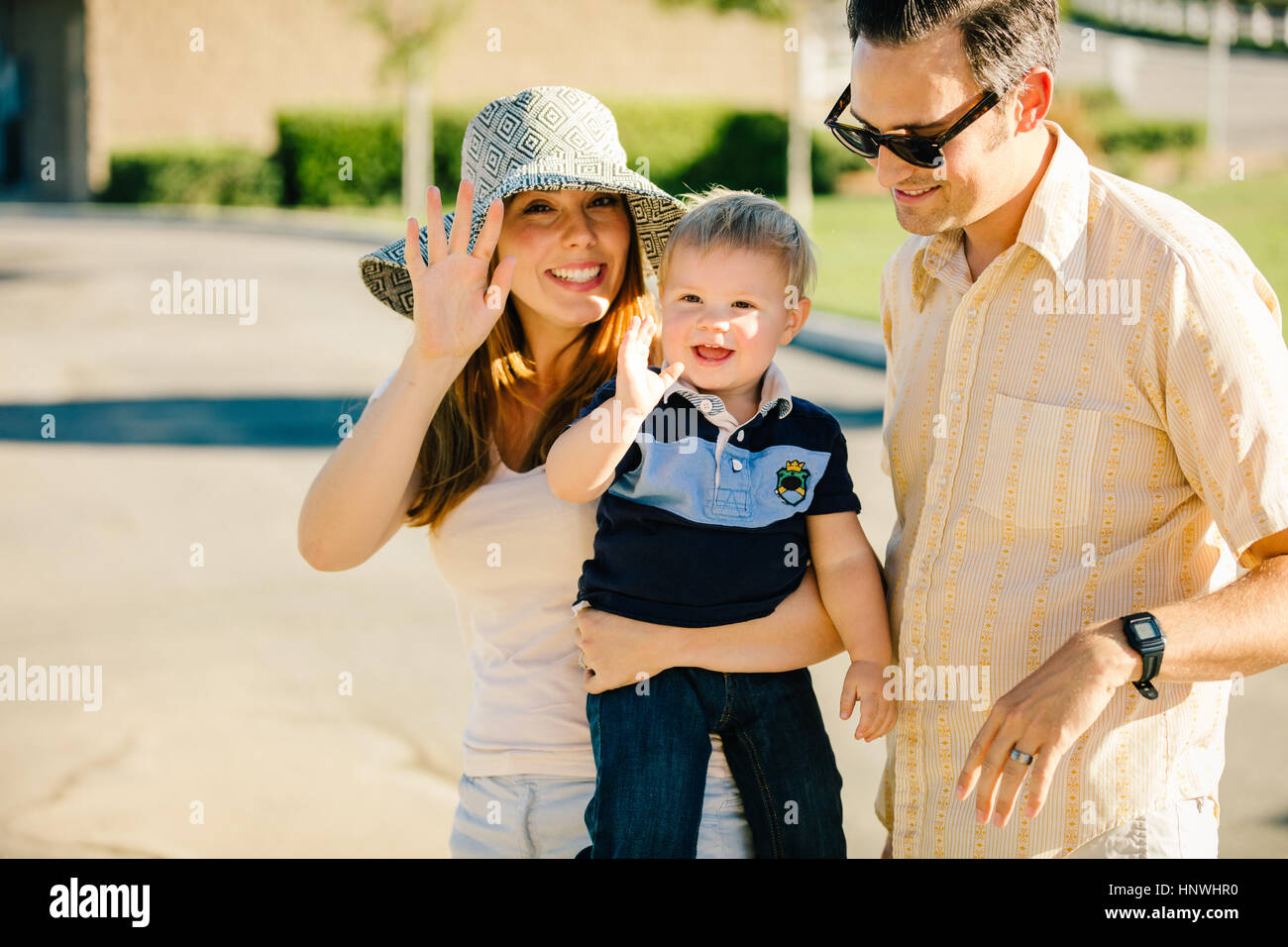 Young family standing together outdoors, mother and young son waving Stock Photo