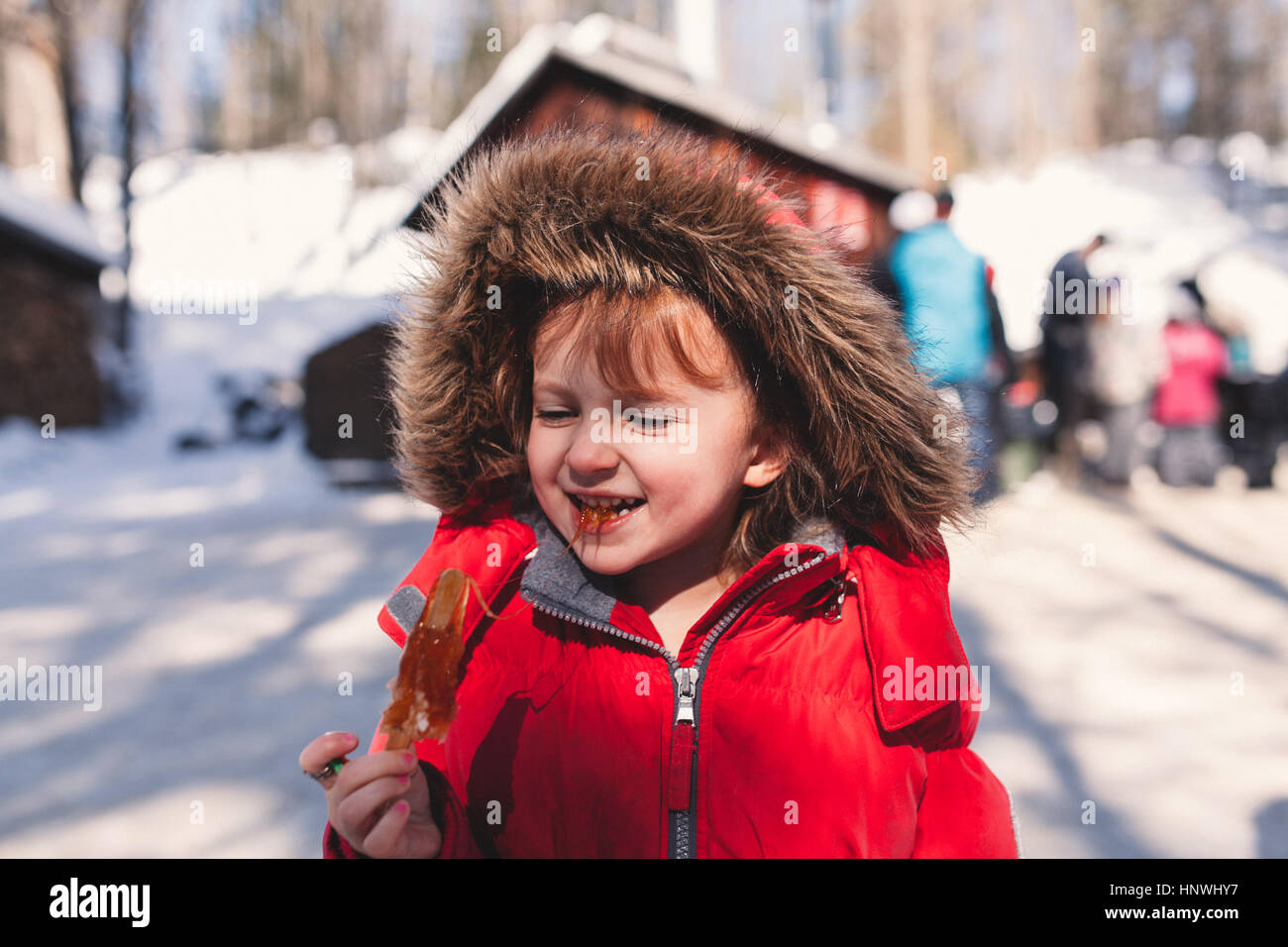 Girl in fur hood eating sticky lolly Stock Photo