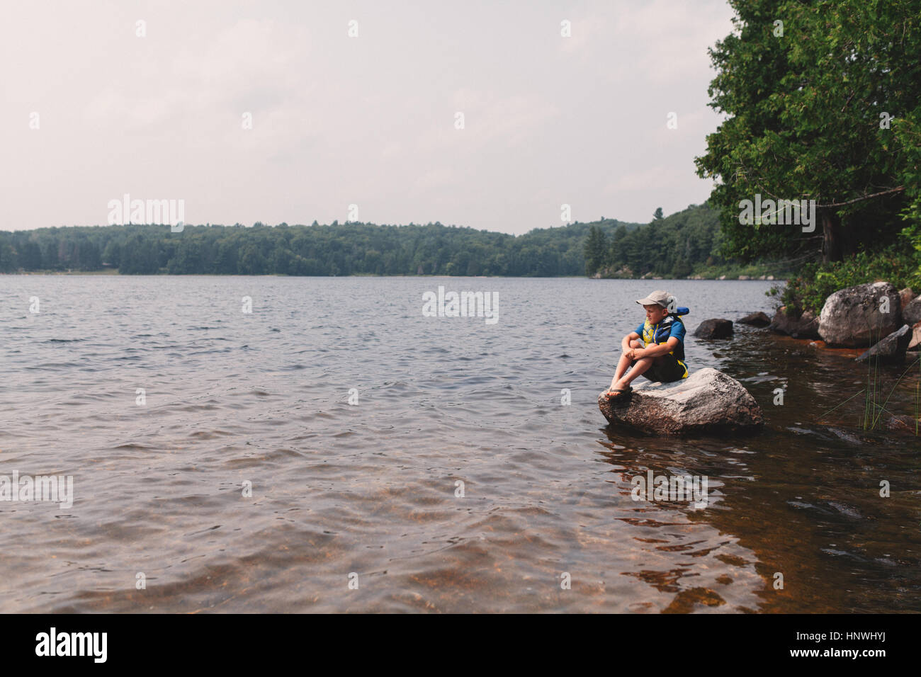 Boy sitting on rock at the edge of a lake Stock Photo - Alamy