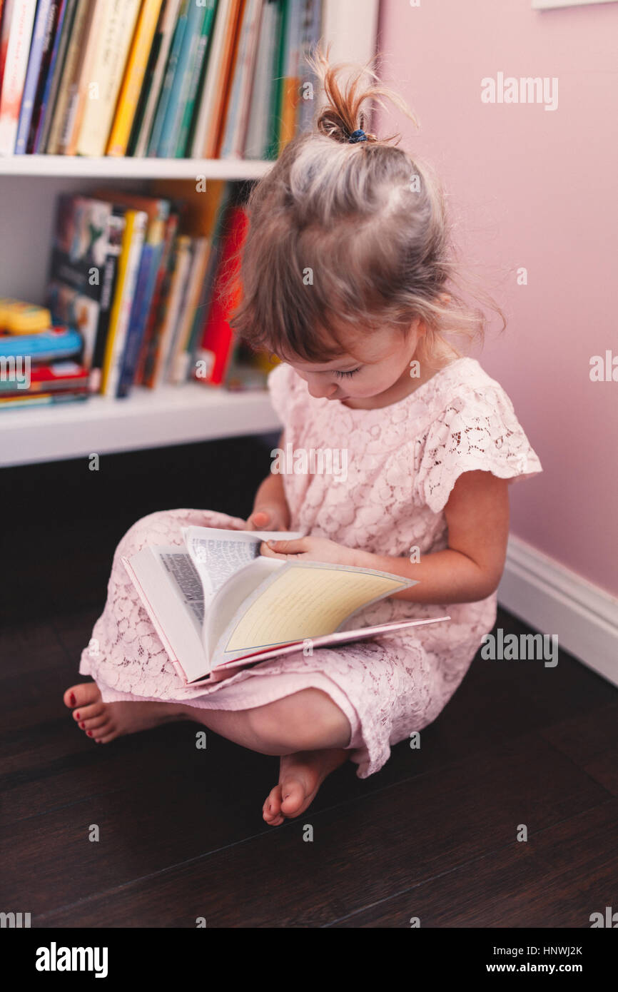 Girl sitting on playroom floor reading book Stock Photo