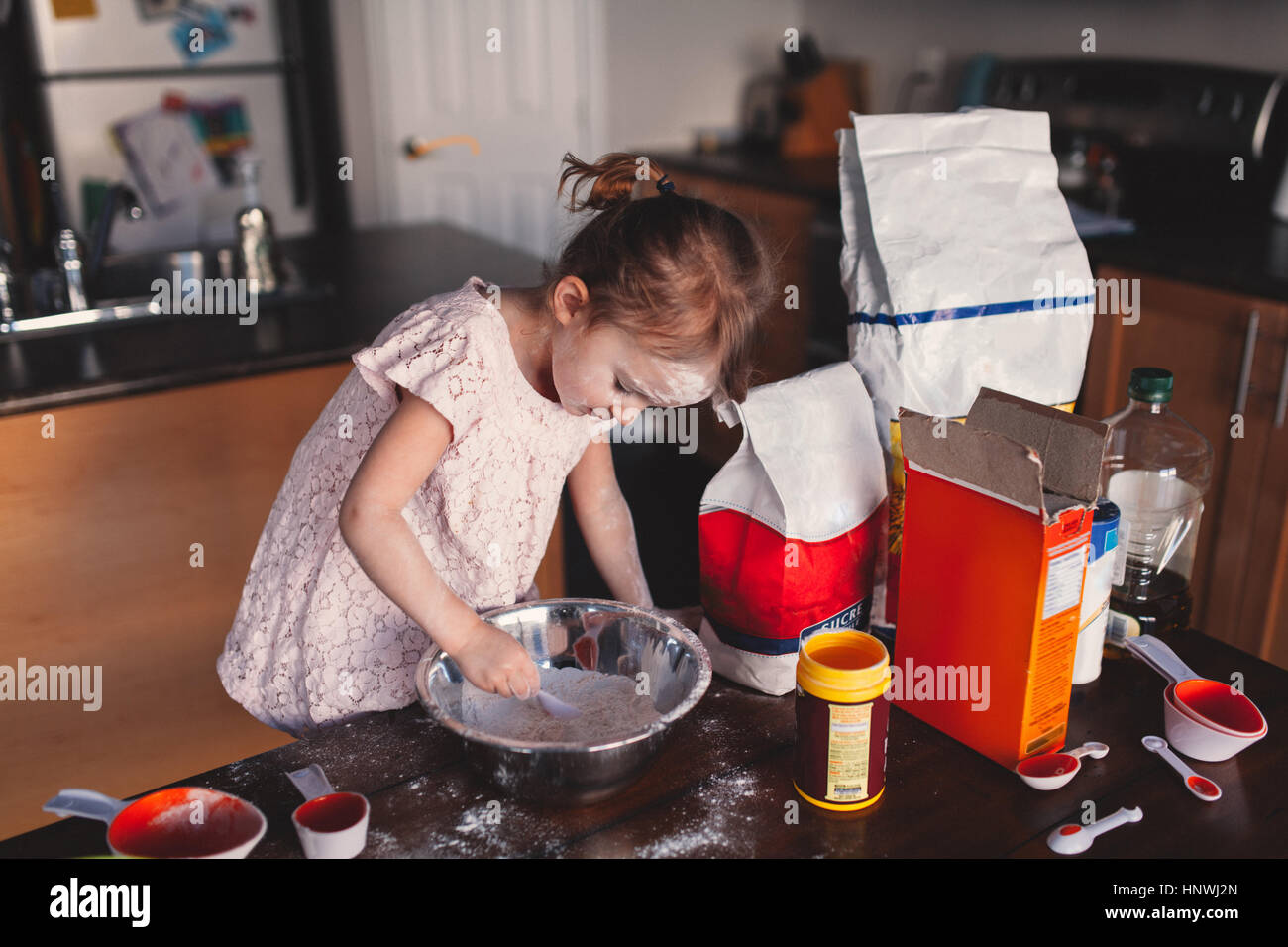 Messy girl in kitchen stirring bowl of flour Stock Photo