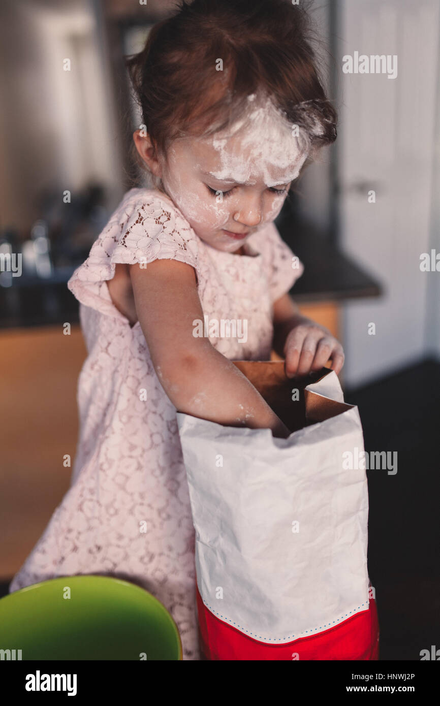 Messy girl in kitchen reaching into bag of flour Stock Photo