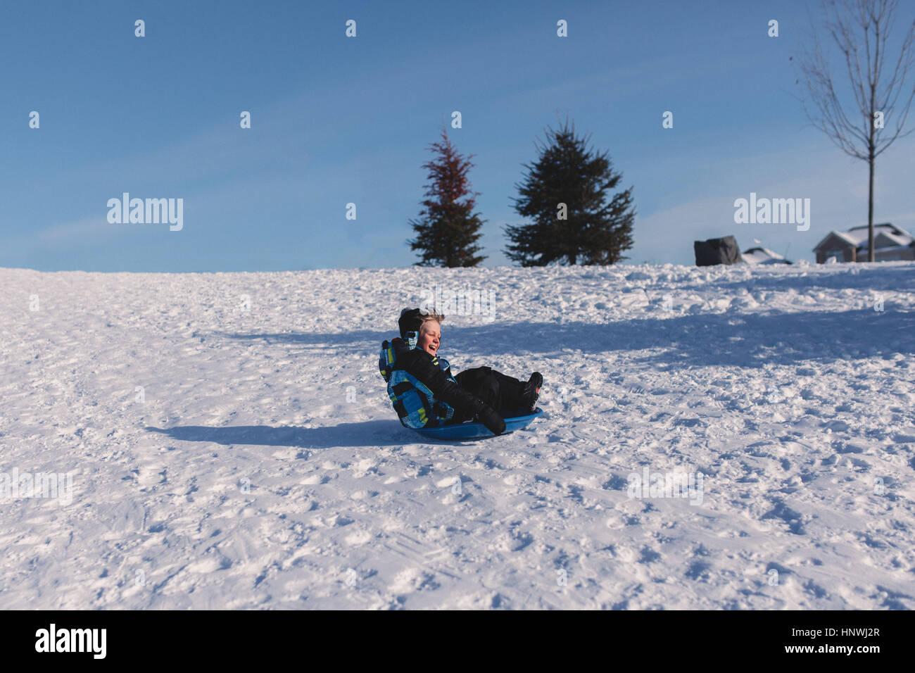 Boy in knit hat tobogganing down snow covered hill Stock Photo