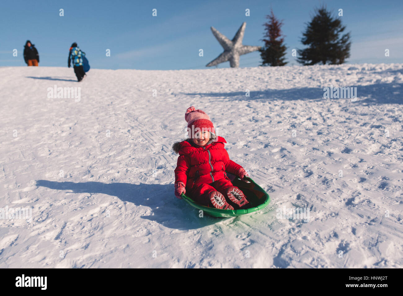 Girl in red knit hat tobogganing down snow covered hill Stock Photo