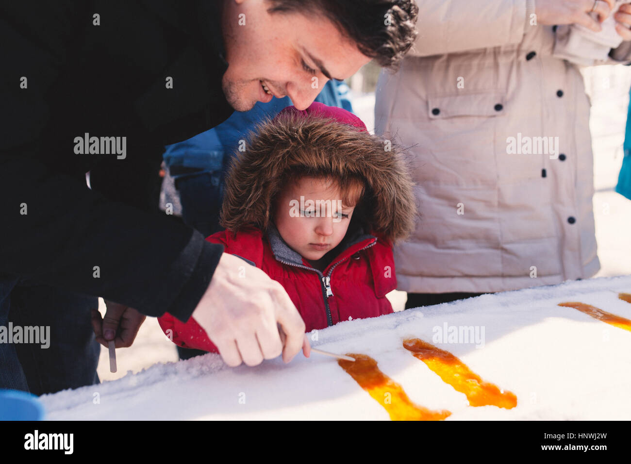 Girl in fur hood with father making lolly in snow ice Stock Photo