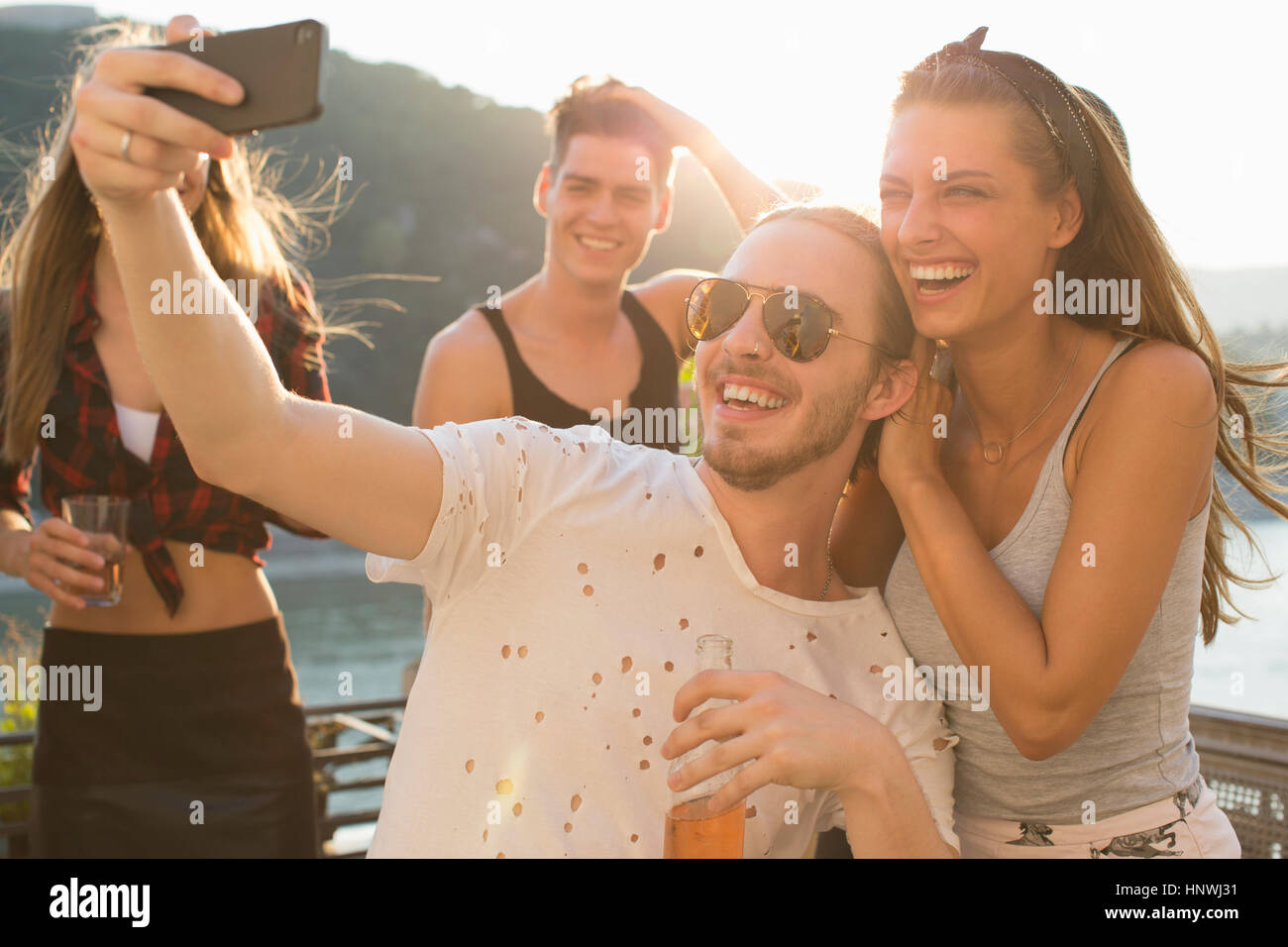 Young man taking selfie with female friend at waterfront roof terrace party, Budapest, Hungary Stock Photo
