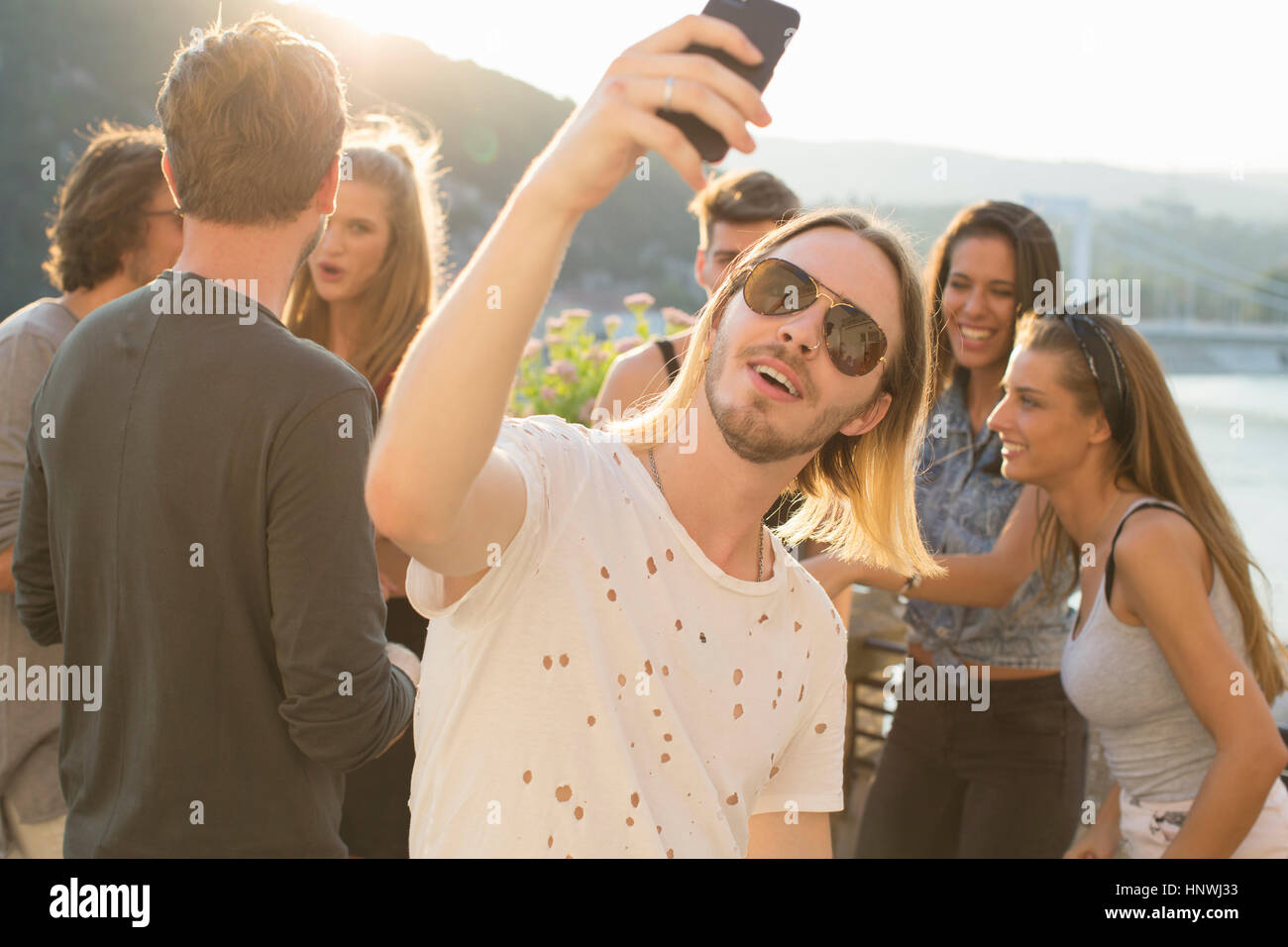 Young man taking selfie at waterfront roof terrace party, Budapest, Hungary Stock Photo