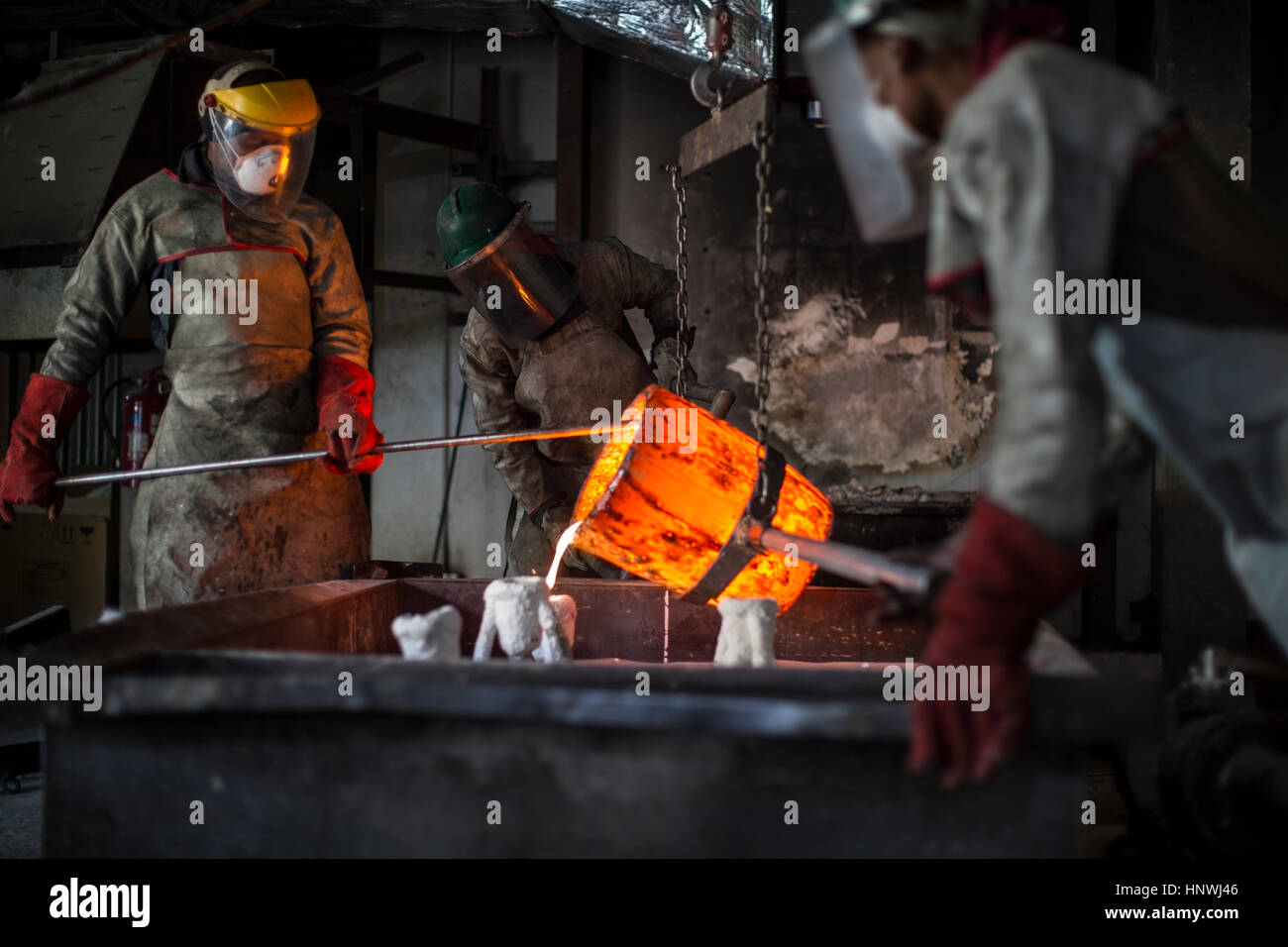 Metalworkers working in foundry, pouring molten bronze Stock Photo