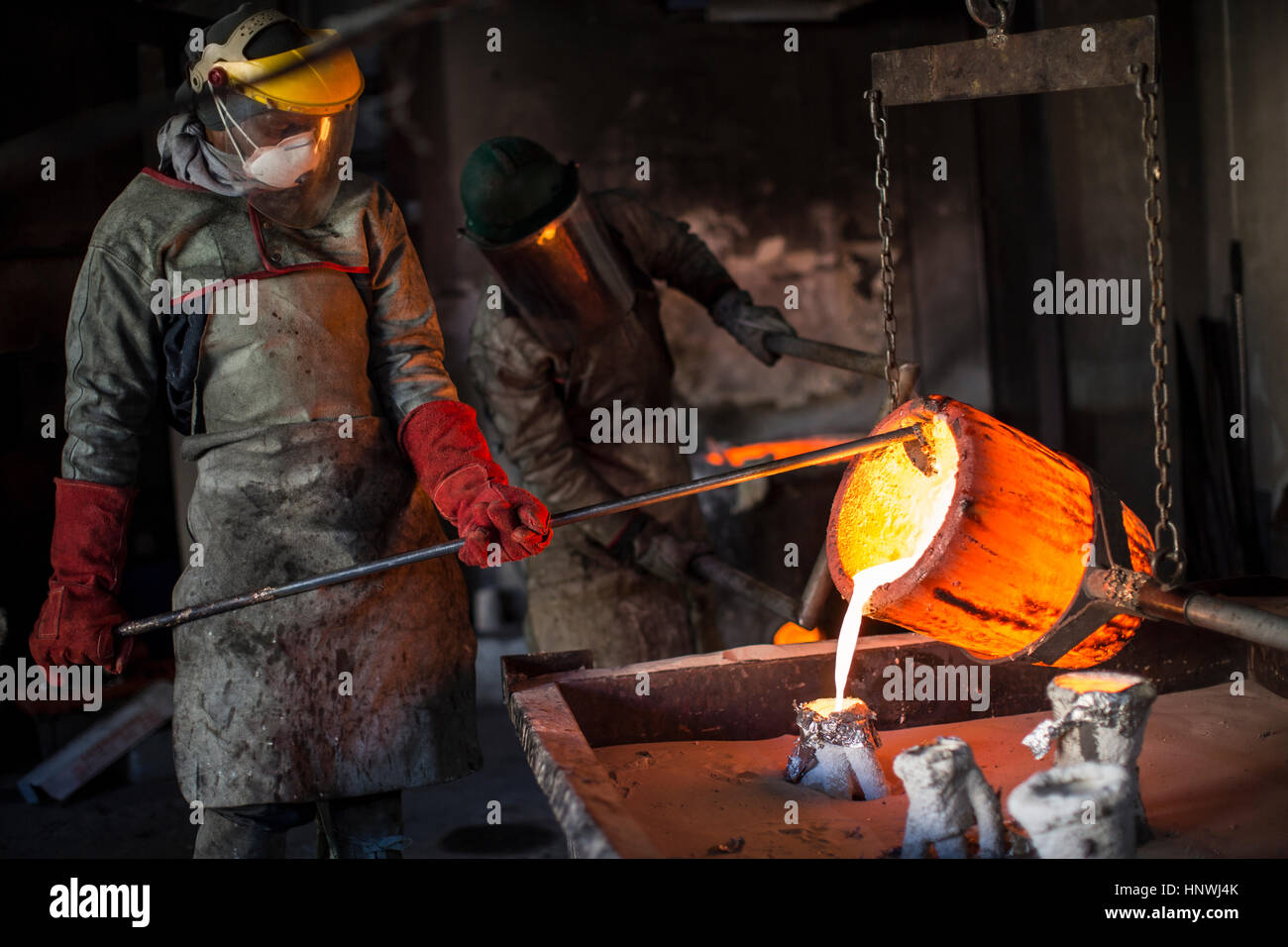 Metalworkers working in foundry, pouring molten bronze Stock Photo