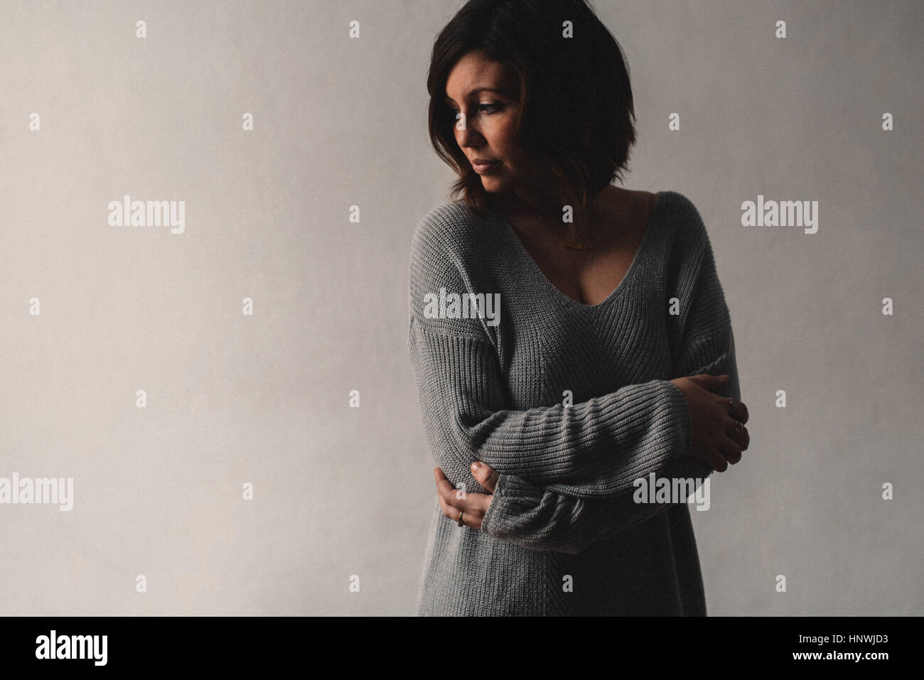 Woman standing with arms crossed, grey wall background Stock Photo