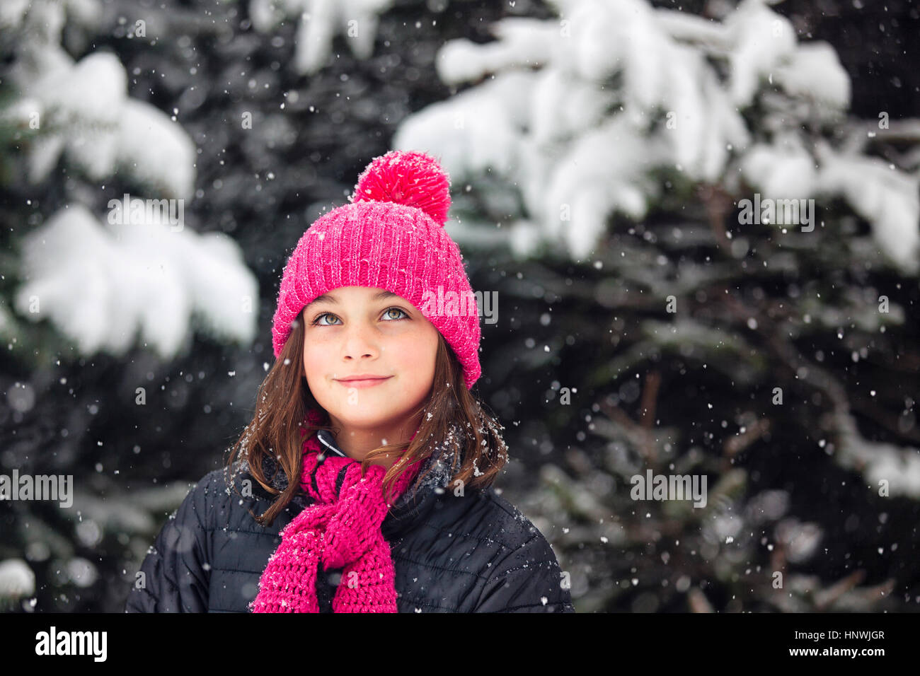 Girl in pink knitted hat looking up at falling snow Stock Photo