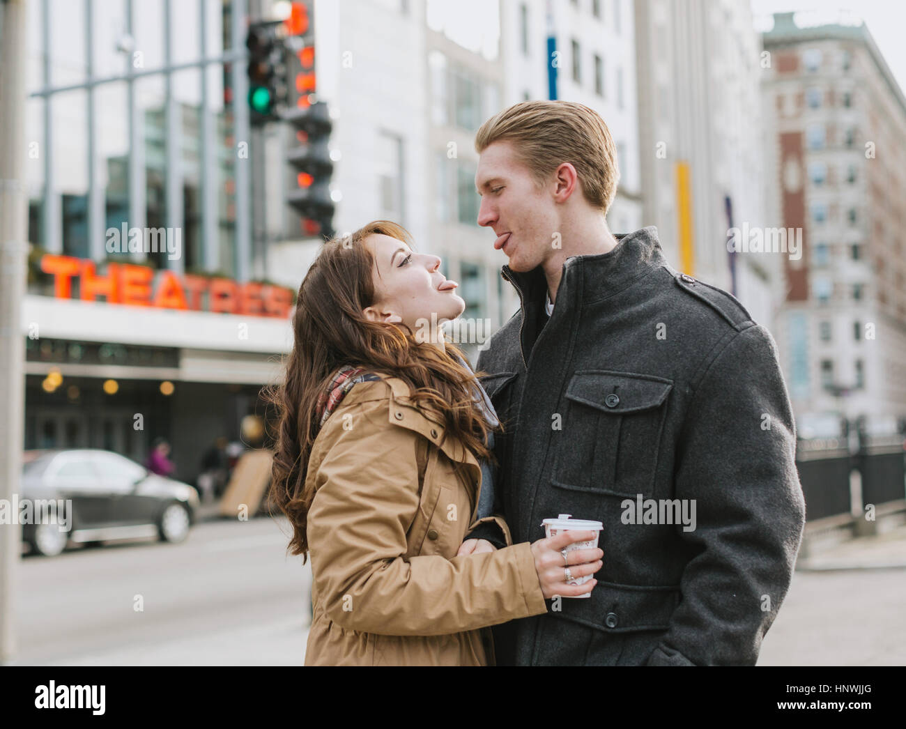 Young couple standing in street, face to face, sticking out tongues Stock Photo