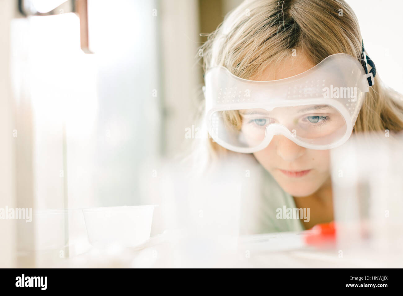 Girl doing science experiment, watching through safety goggles Stock Photo