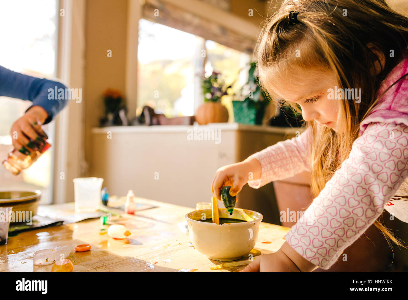 Girl doing science experiment, dropping green liquid into bowl Stock Photo
