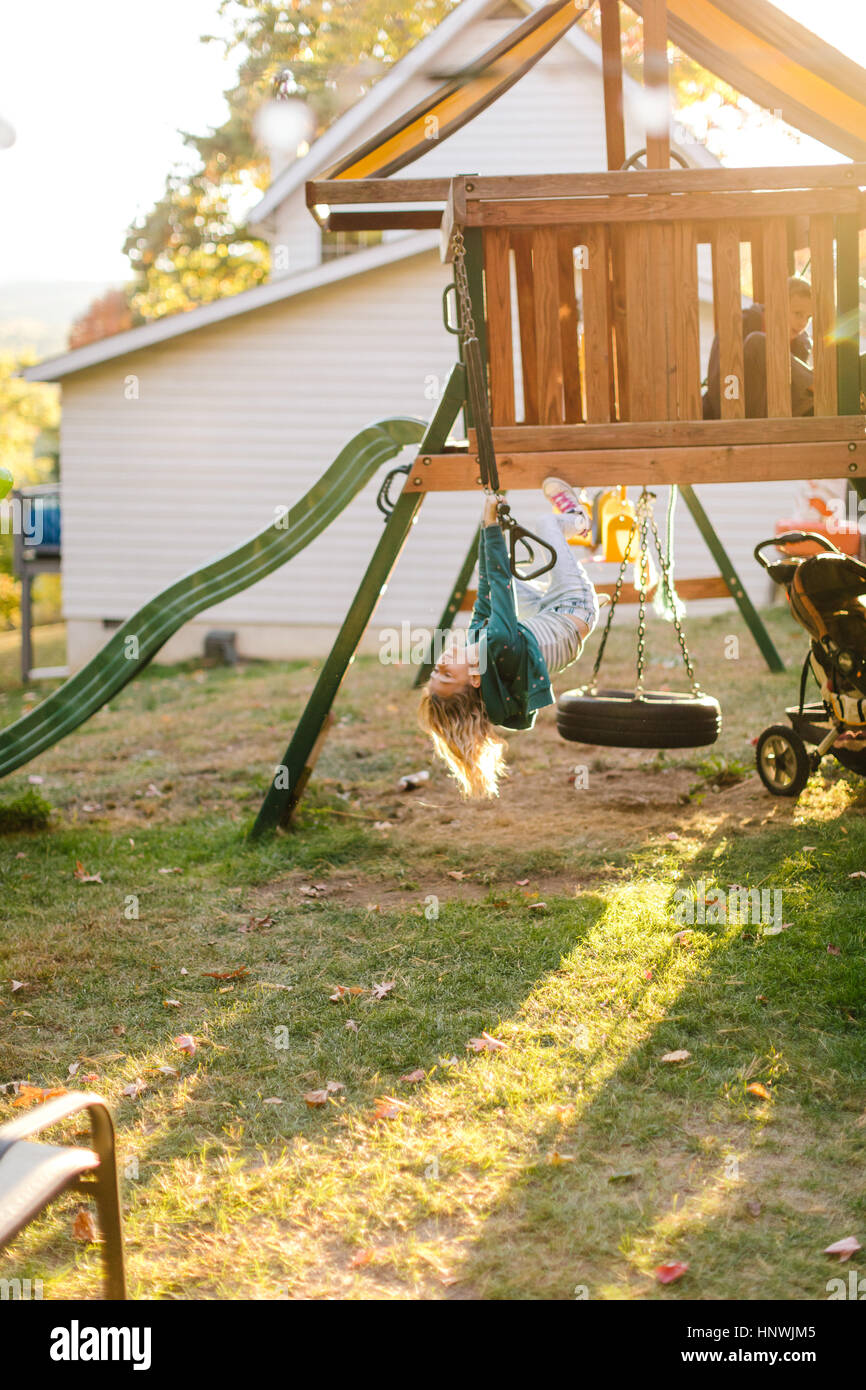 Girl hanging upside down on playground equipment in garden Stock Photo