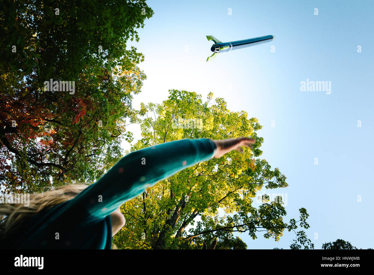 Low angle view of girl watching toy rocket flying toward blue sky Stock Photo