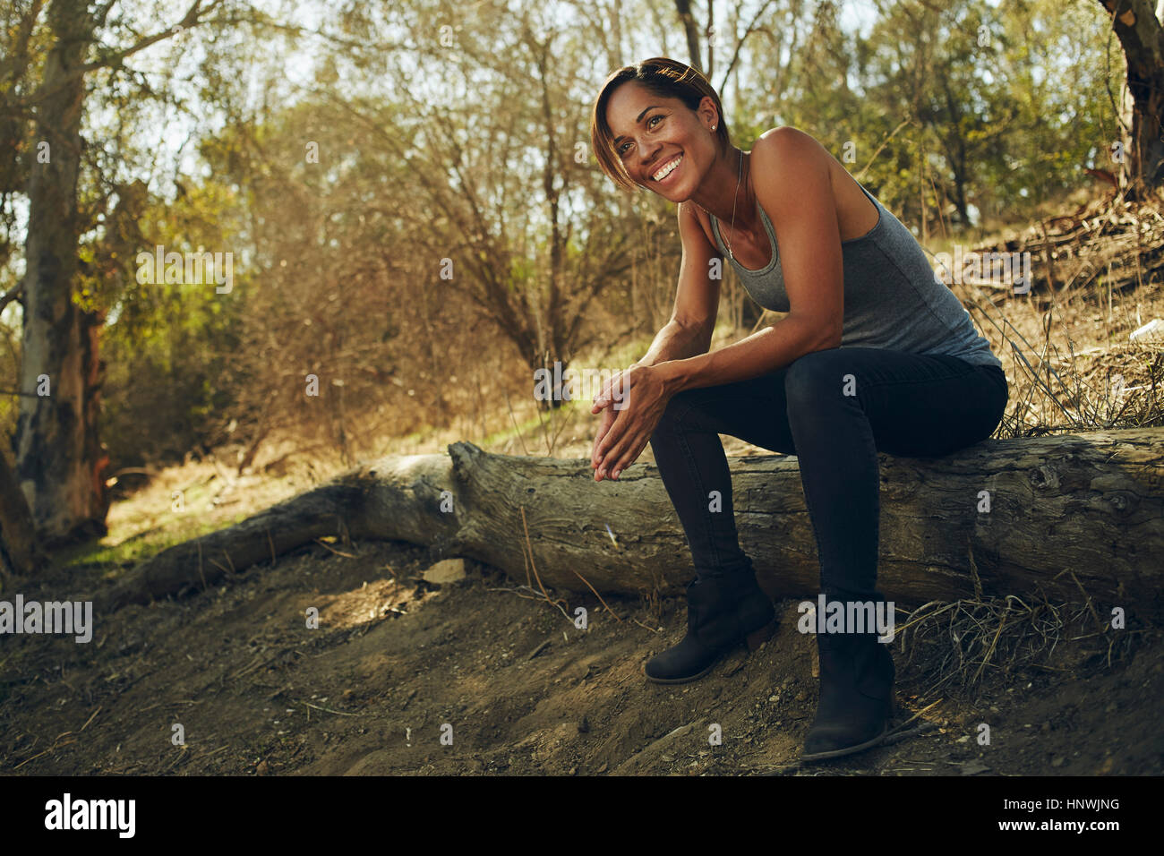 Happy mid adult woman sitting on hillside log Stock Photo