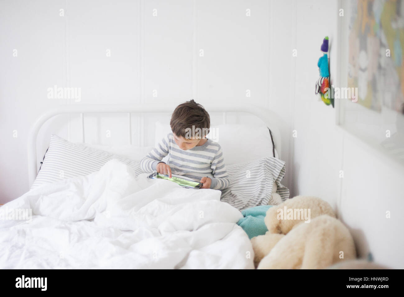 Boy sitting up in bed playing video game on digital tablet Stock Photo