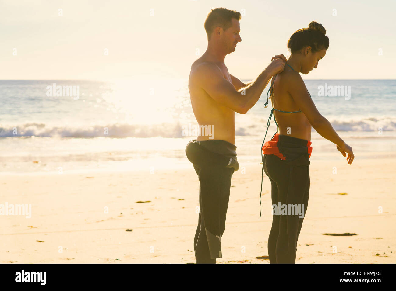 Man helping girlfriend put on wetsuit at Newport Beach, California, USA Stock Photo
