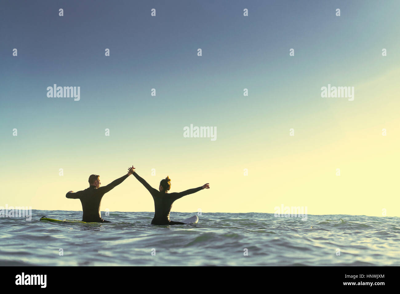 Surfing couple on surfboards holding hands in sea, Newport Beach, California, USA Stock Photo
