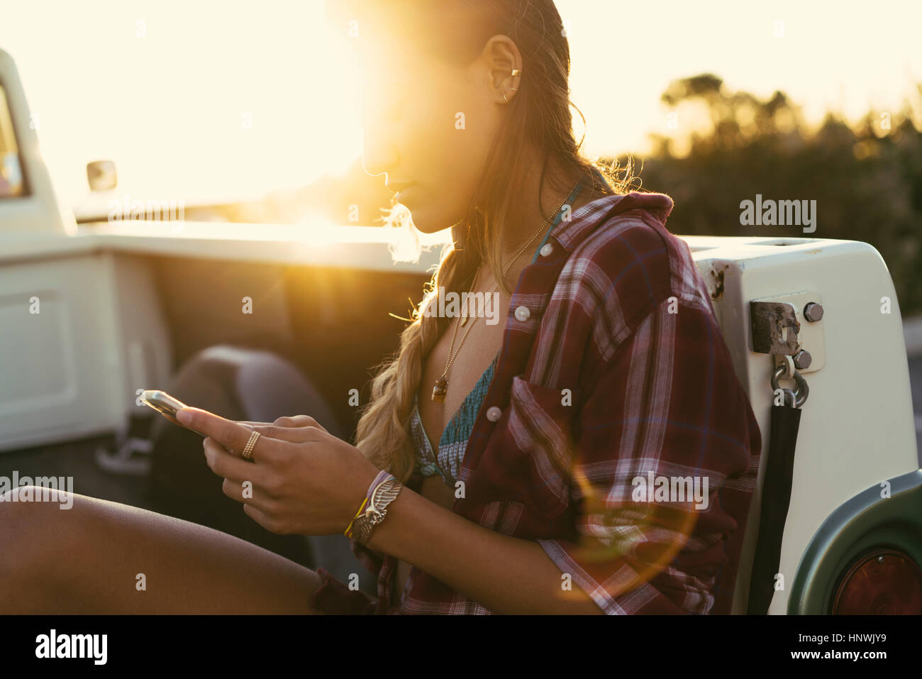 Young woman looking at smartphone from back of pickup truck at Newport Beach, California, USA Stock Photo