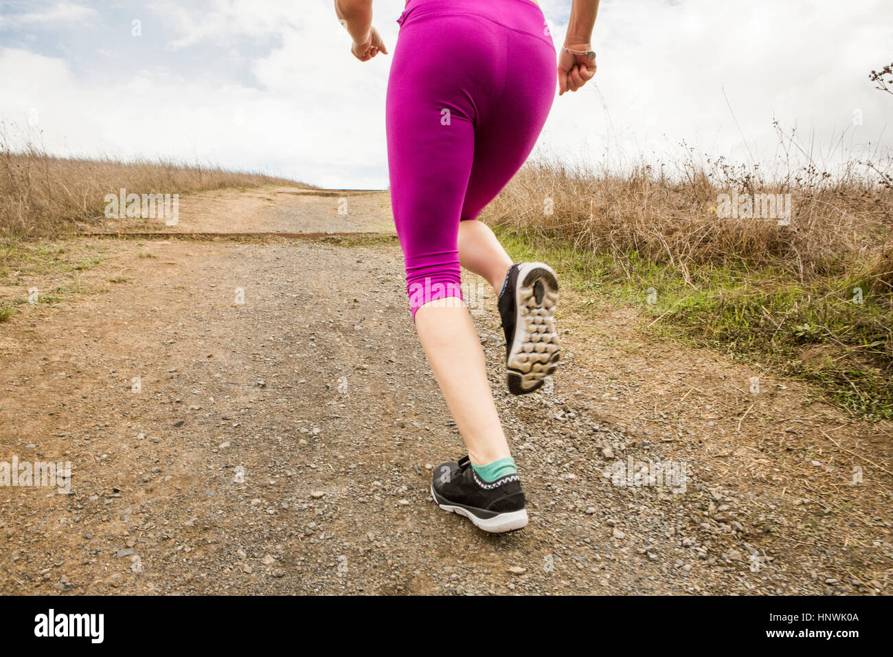 Waist down rear view of female runner running up dirt track Stock Photo
