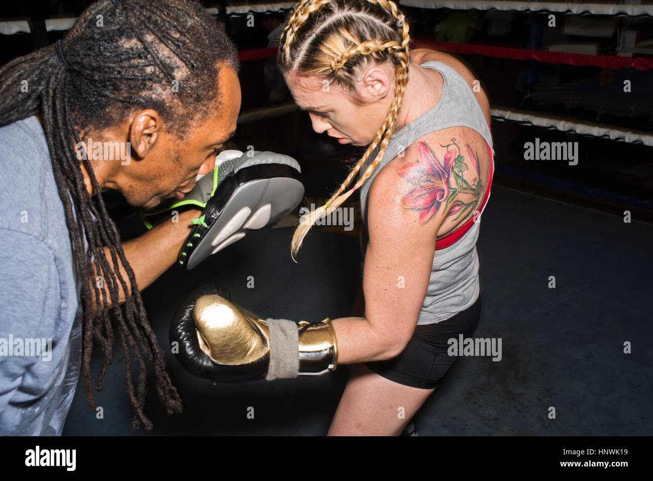 Female boxer punching trainer's boxing mitt in boxing ring Stock Photo