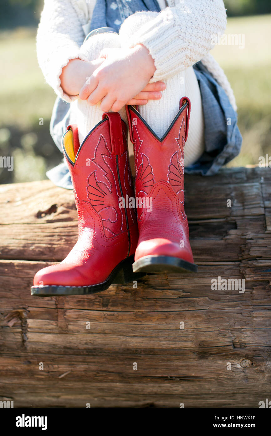Neck down view of girl sitting on log wearing red cowboy boots Stock Photo