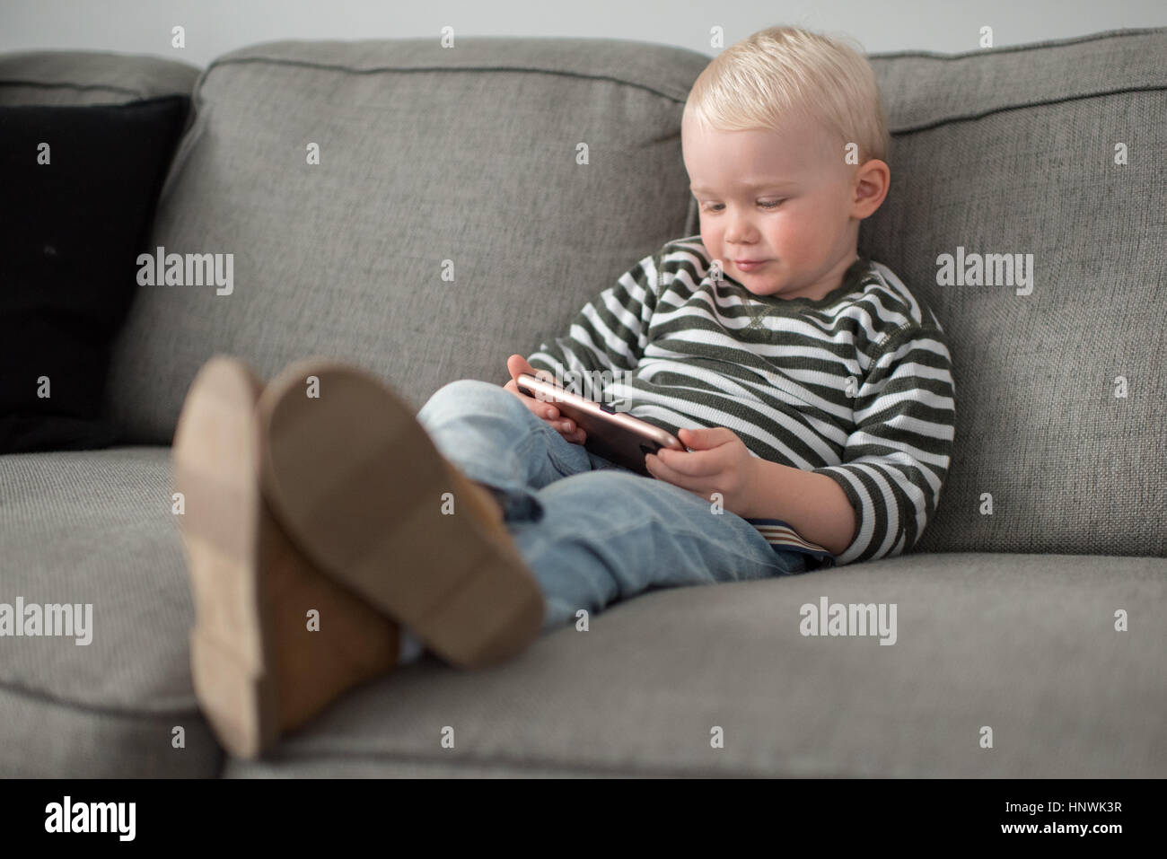 Young boy sitting on sofa, looking at smartphone Stock Photo - Alamy