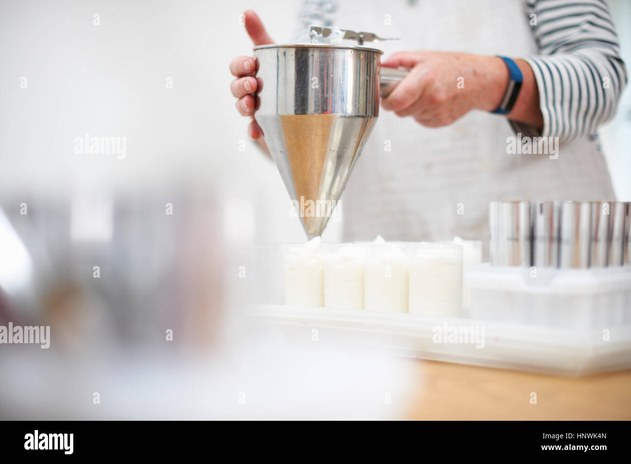 Senior woman in kitchen, using pancake funnel to dispense cream, homemade cosmetics, into pots, mid section Stock Photo