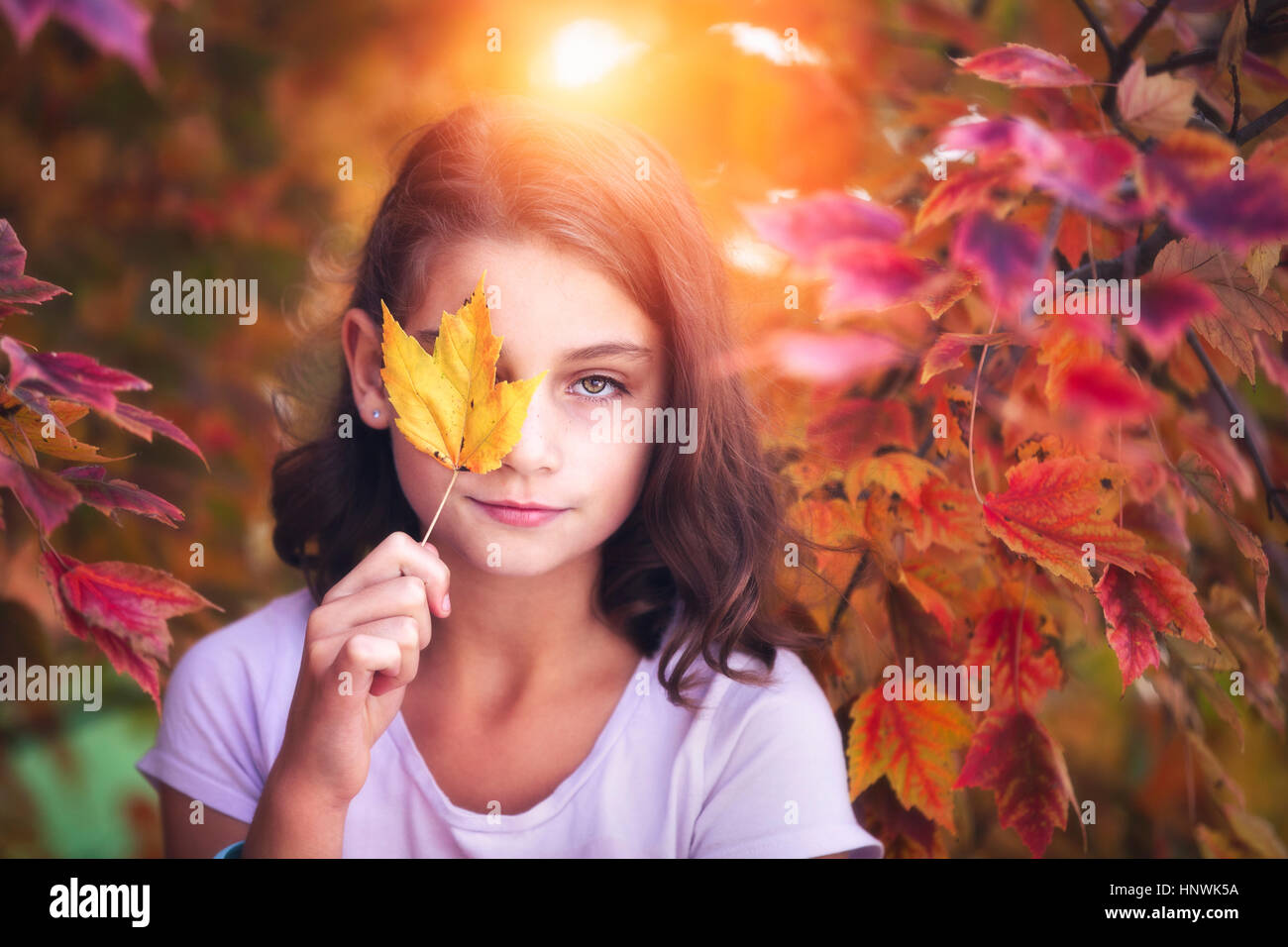 Portrait of young girl in rural setting, holding leaf in front of eye ...