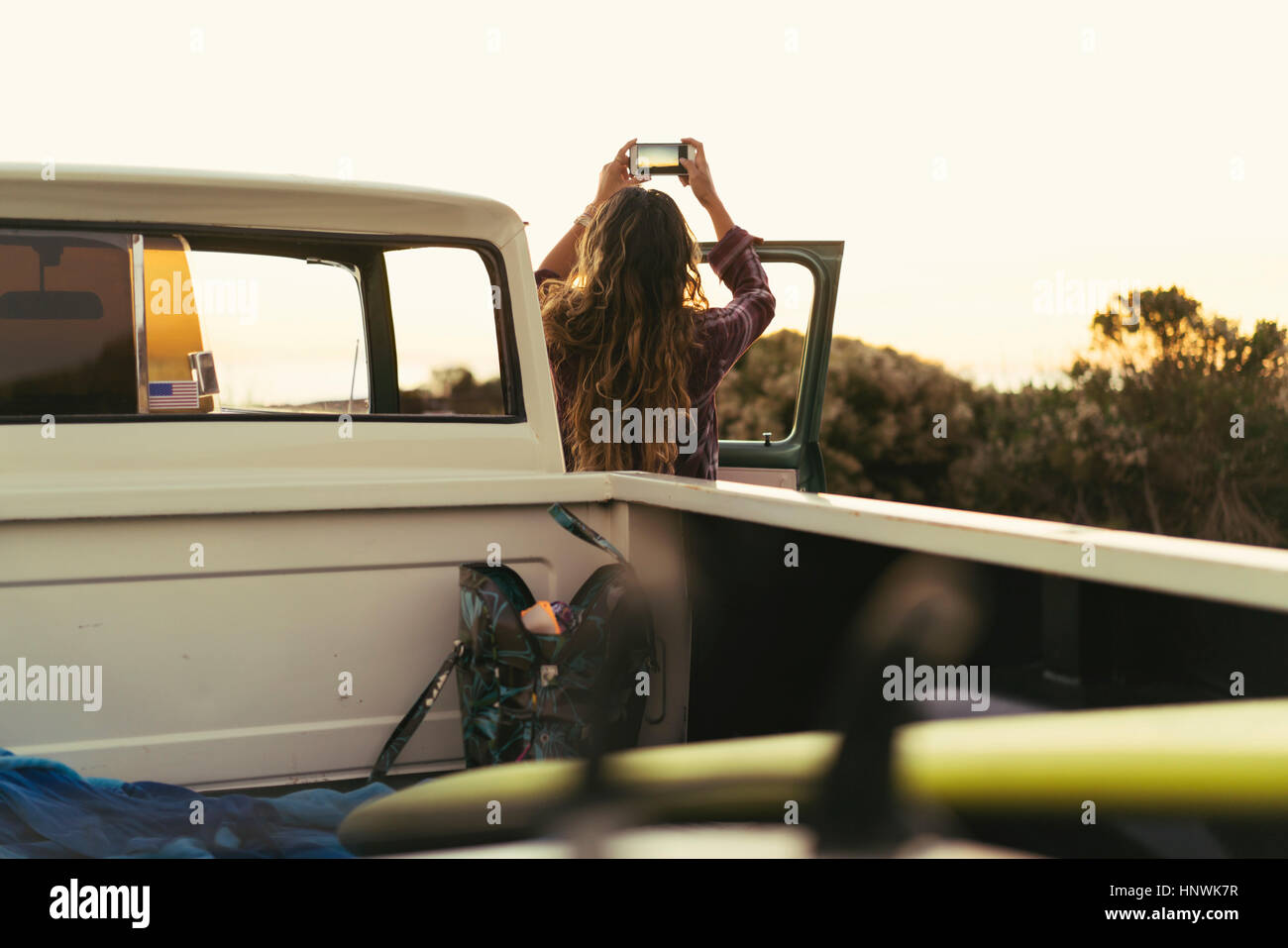 Rear view of  young woman with pickup truck photographing coast at Newport Beach, California, USA Stock Photo