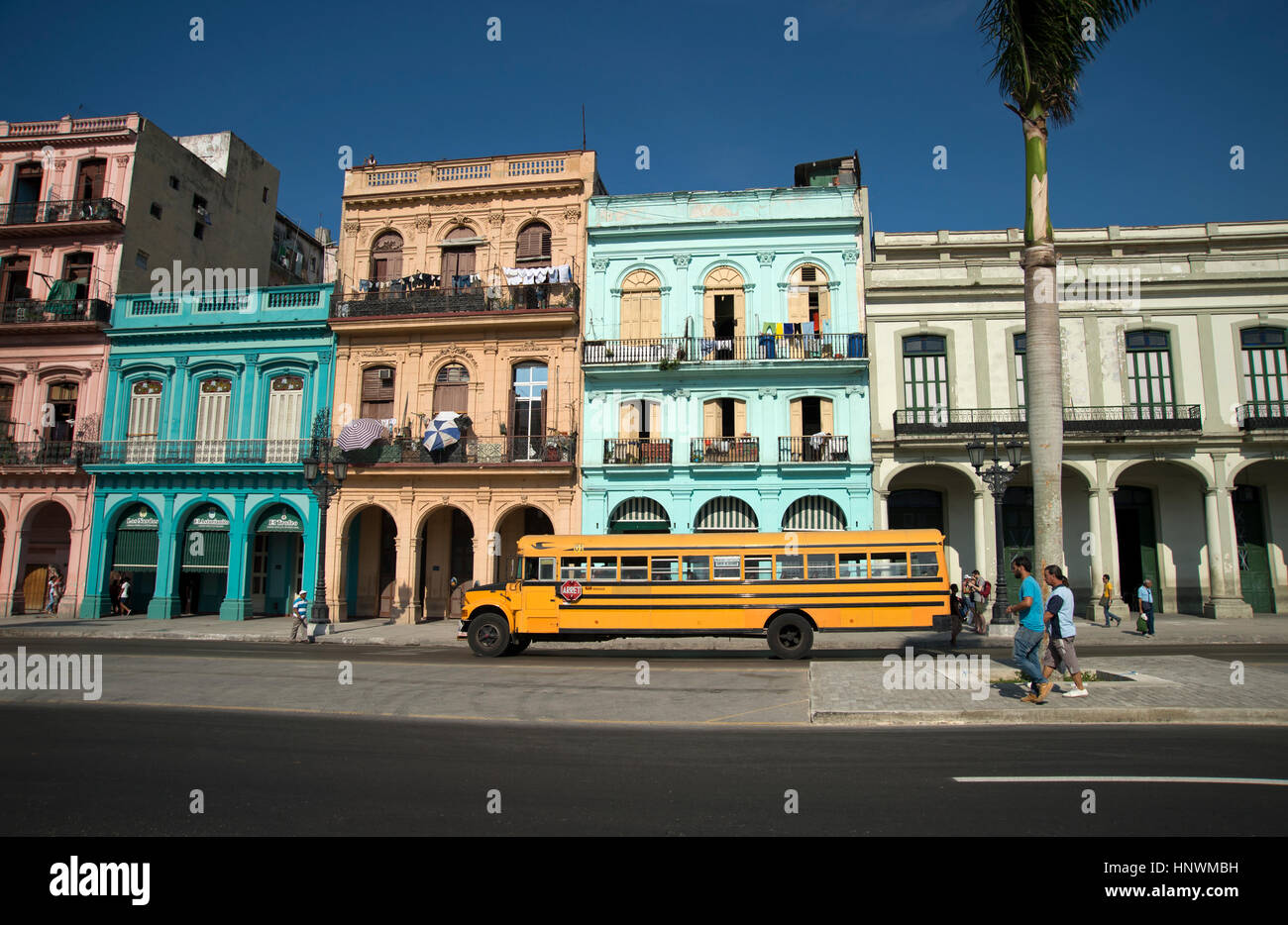 An old American 1950's school bus drives past a row of restored classic buildings in Centro Havana Cuba Stock Photo