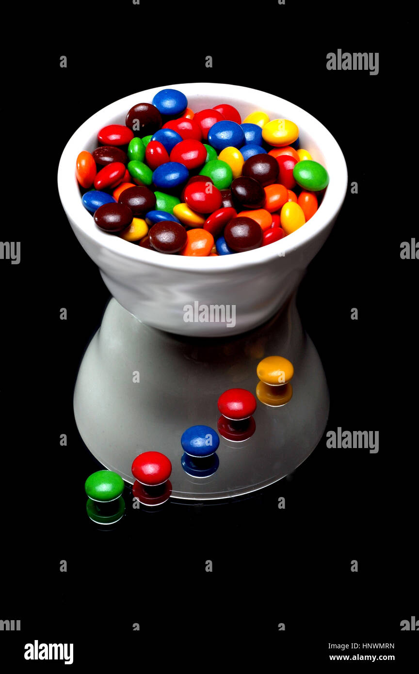 white bowl of m&m's candies with some on table Stock Photo