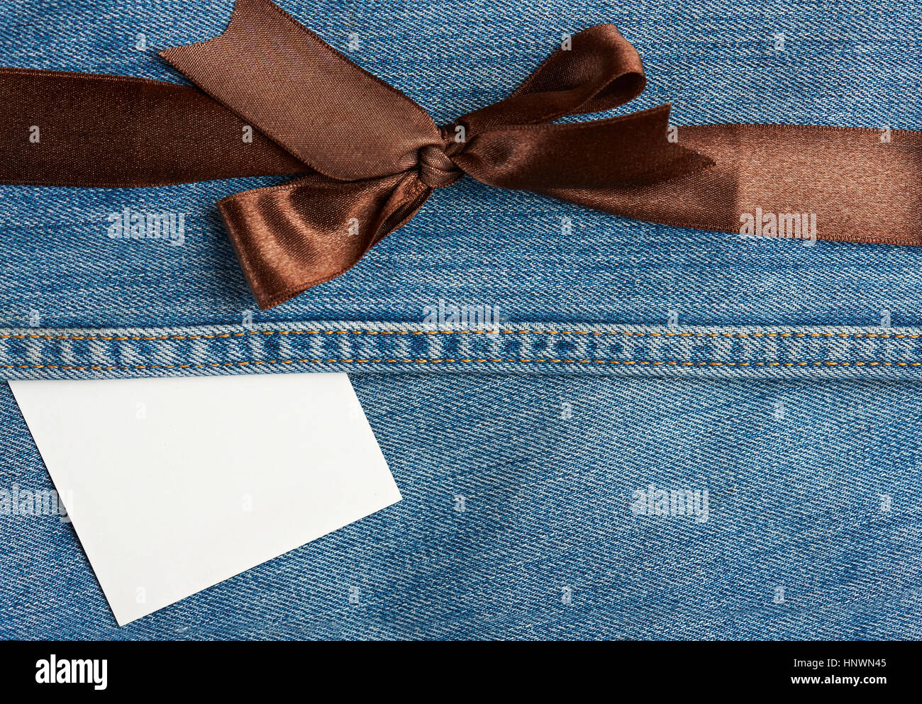Tag and brown ribbon on light blue jeans background Stock Photo
