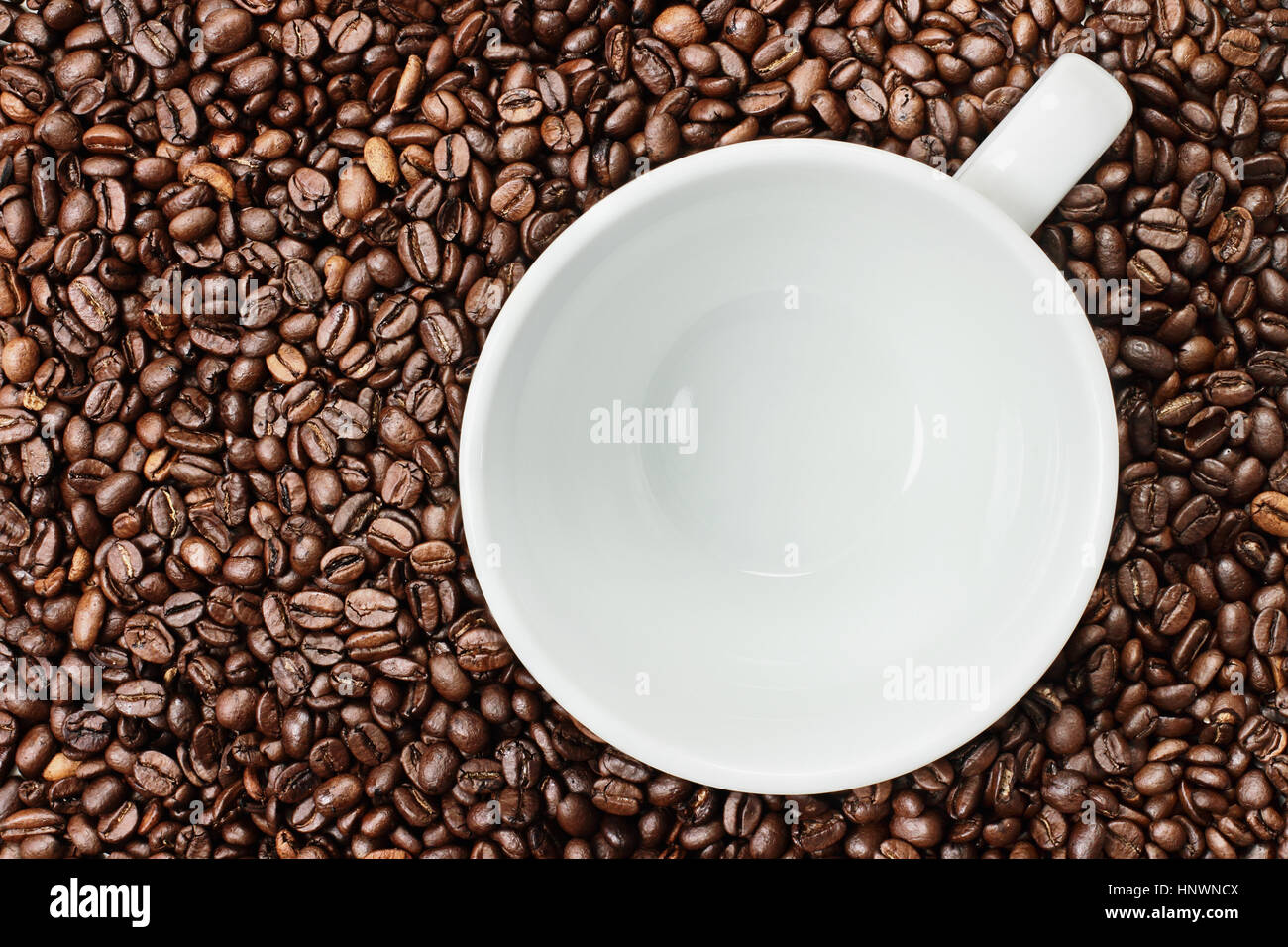 Overhead shot of an empty white cup over over a fresh background of whole coffee beans. Flat lay top view style. Stock Photo