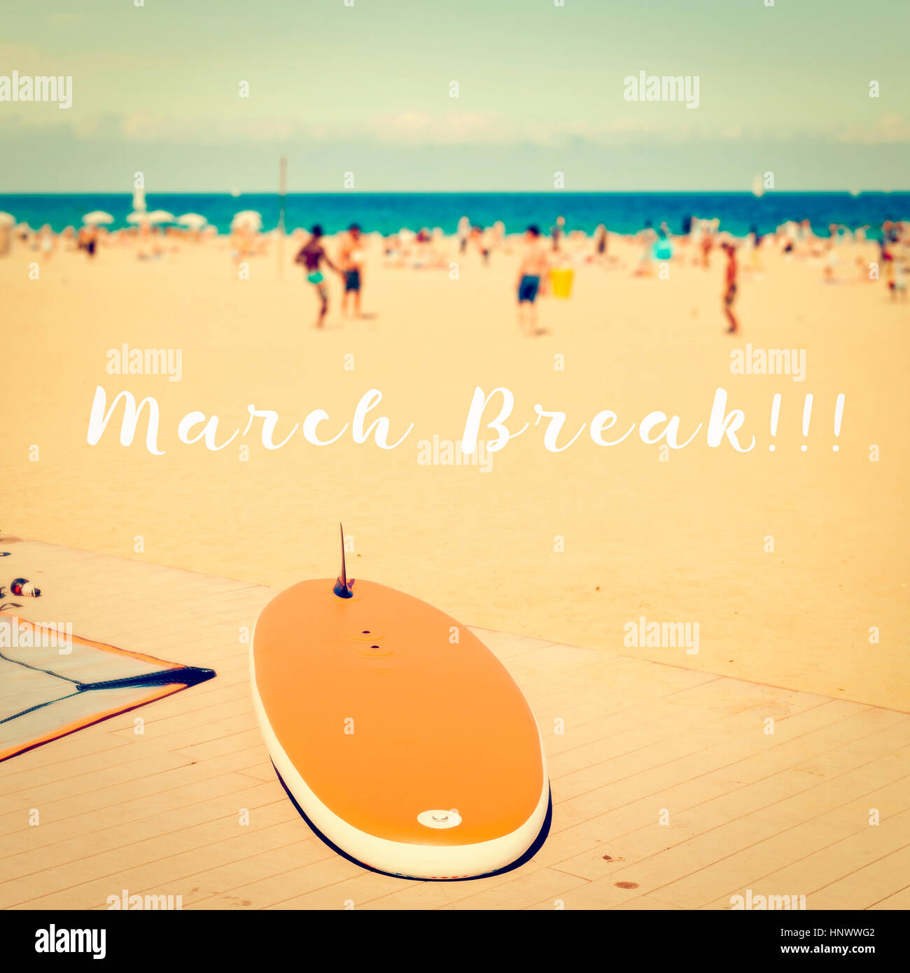 text march break on a blurred picture of a beach with a surfboard in the foreground and unrecognizable people playing beach soccer and other people su Stock Photo