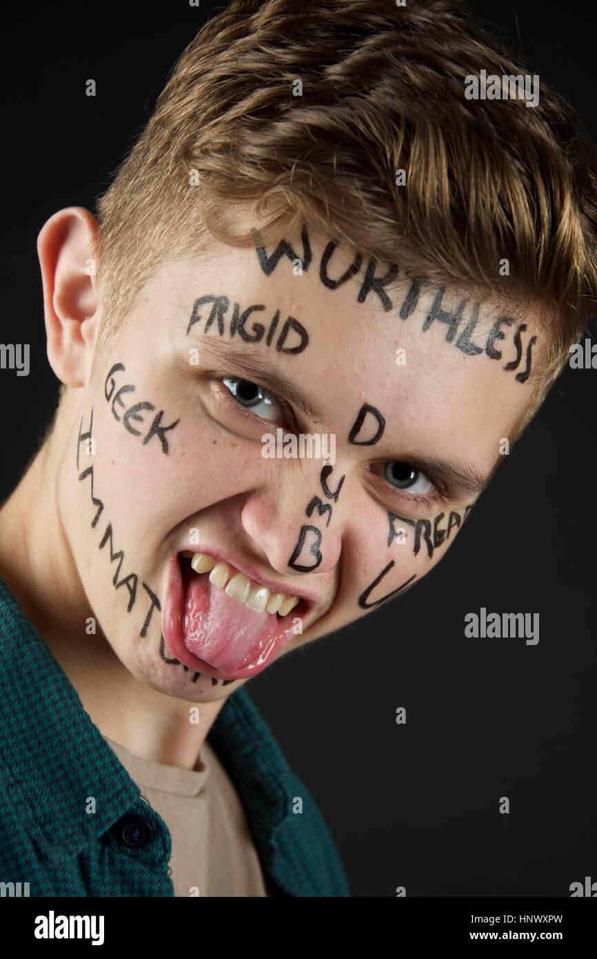 A young boy sticking his tongue out with bruises that has been beaten up with bullying words written on his face. Stock Photo