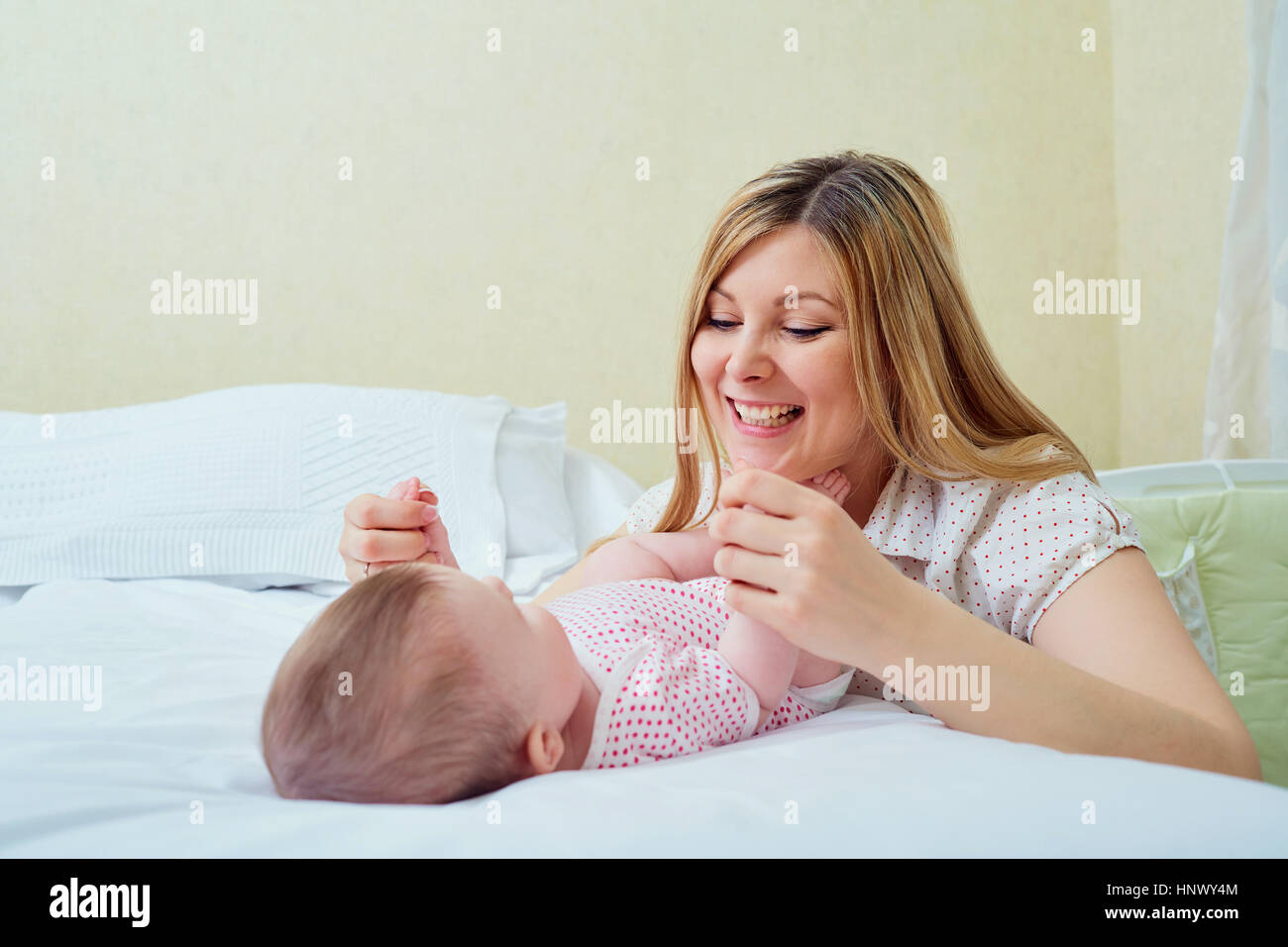 Mother playing with her baby on the bed. Mom smiles to her child Stock Photo