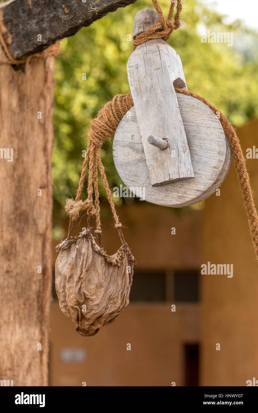 Old pulley and leather water bucket.  Wooden pulley with natural fibre rope holding a leather bucket to collect water from a well in the middle east Stock Photo