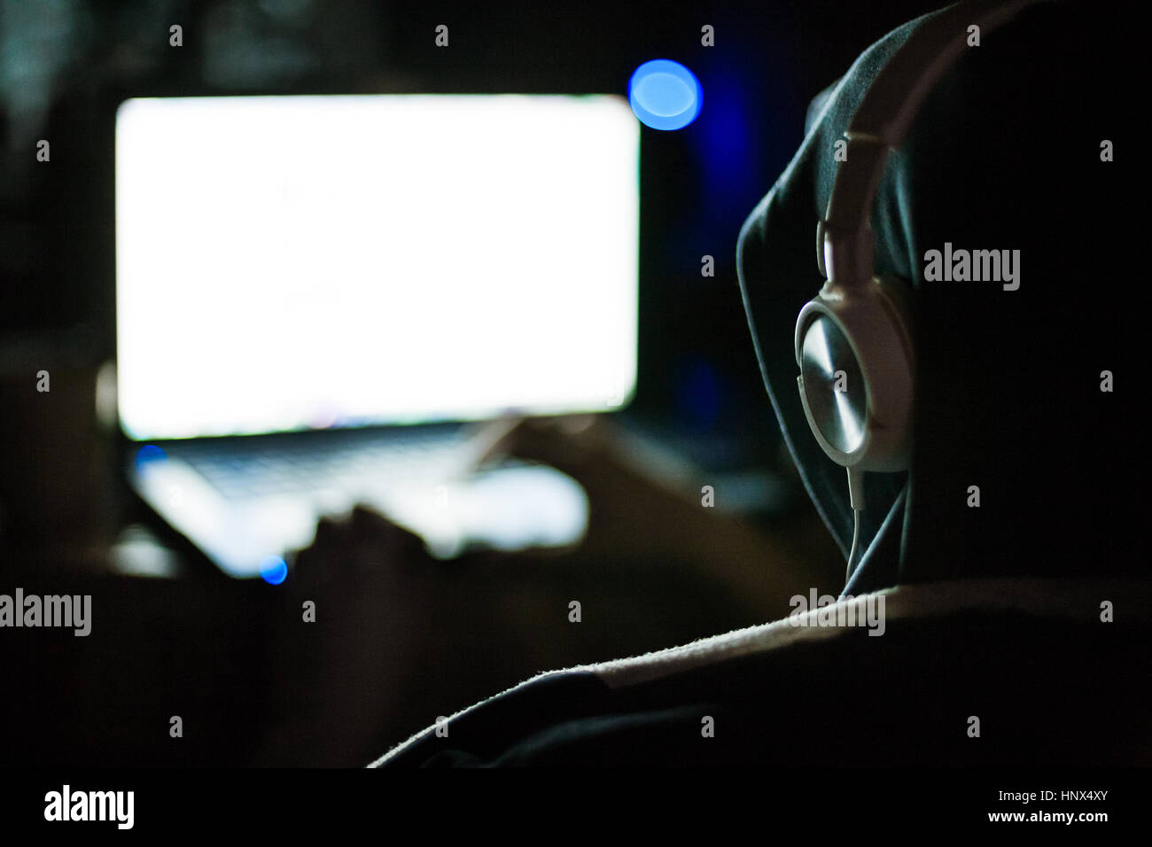 Man hacker in hood and headphones working on laptop in the dark Stock Photo