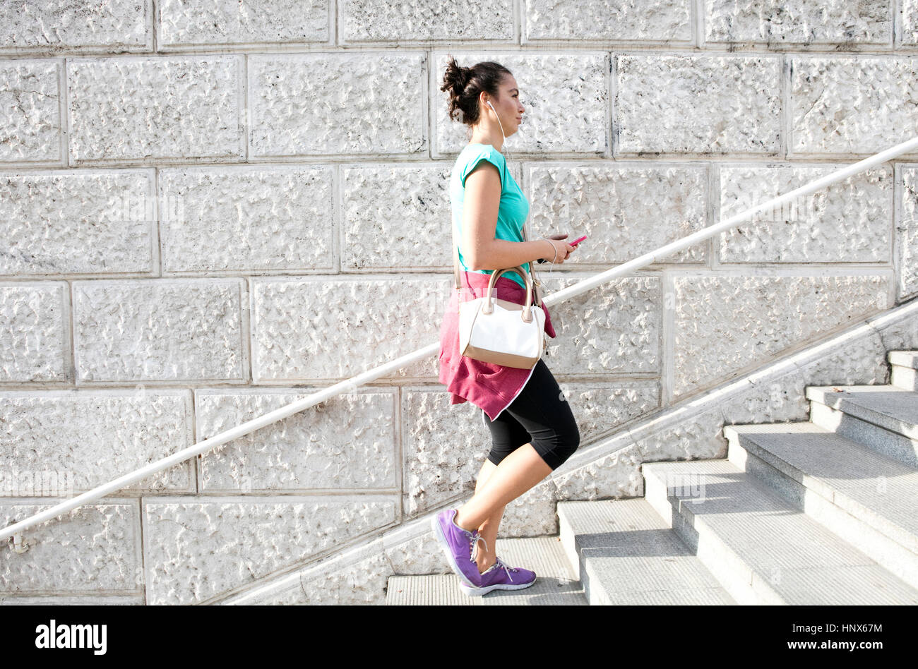 Young woman wearing sports clothing and earphones, walking up steps Stock Photo