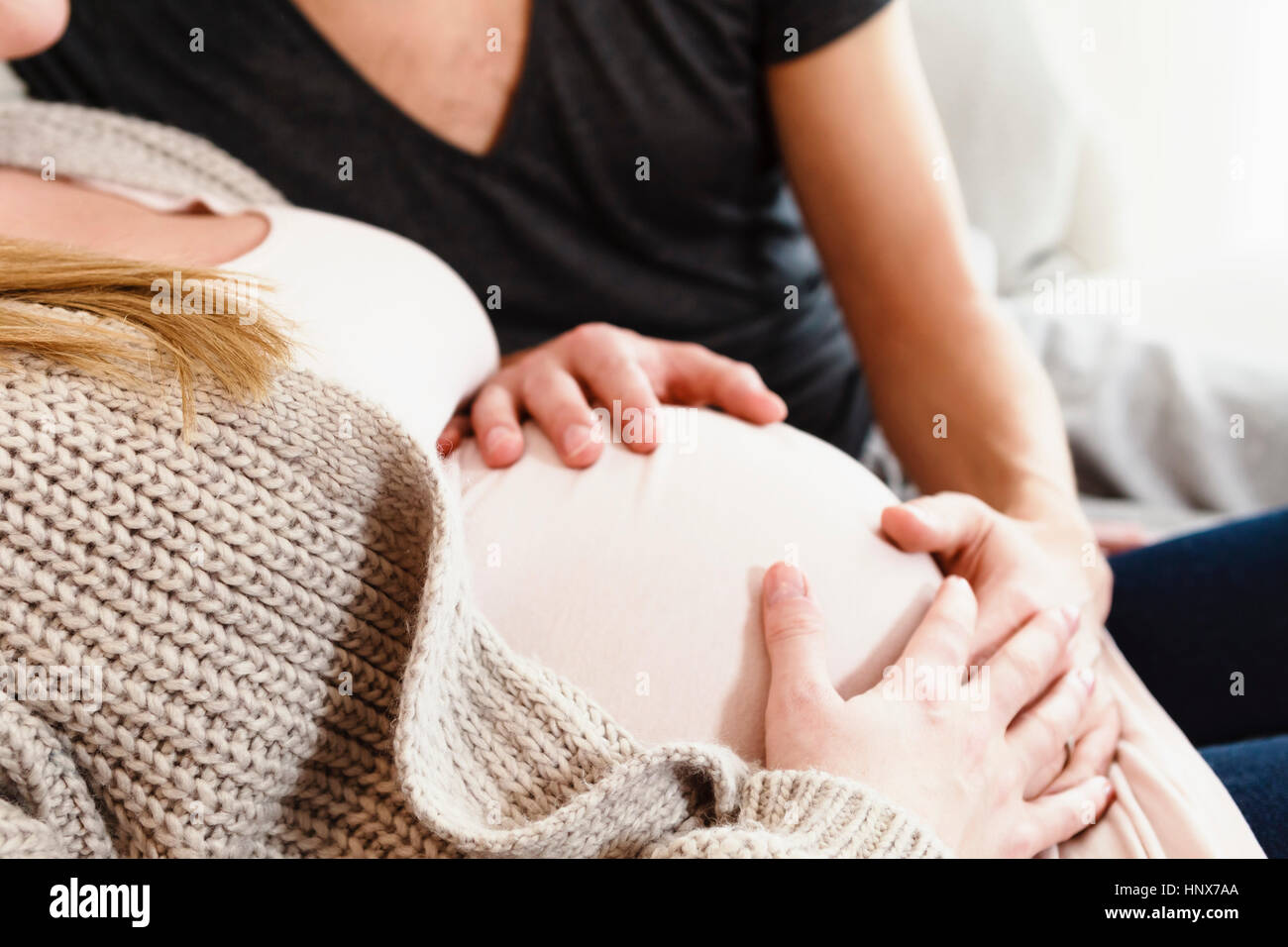 Cropped shot of pregnant mid adult couple touching pregnant stomach on sofa Stock Photo