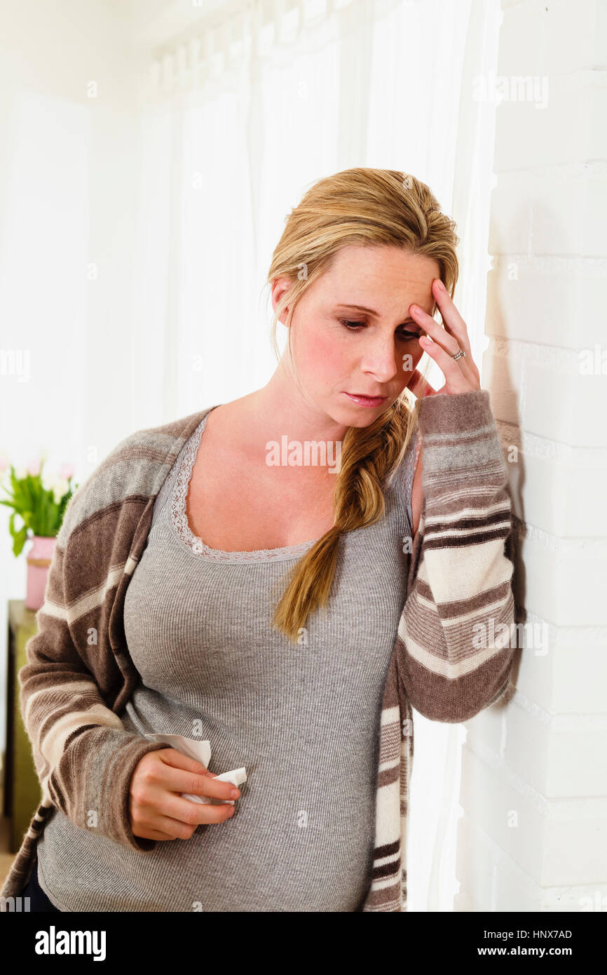 Unwell pregnant woman leaning against living room wall Stock Photo