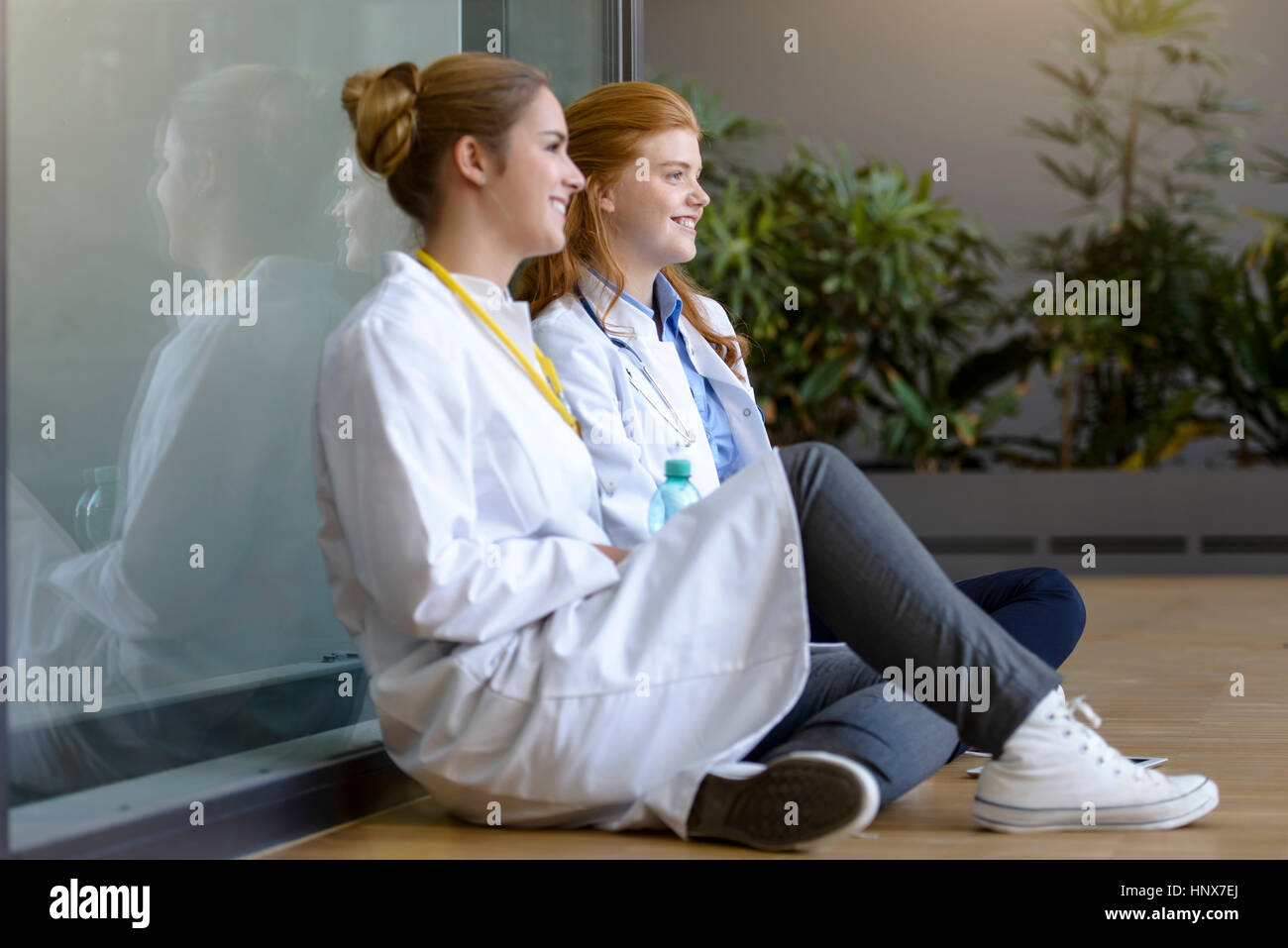 Two young female doctors sitting on floor at hospital entrance Stock Photo
