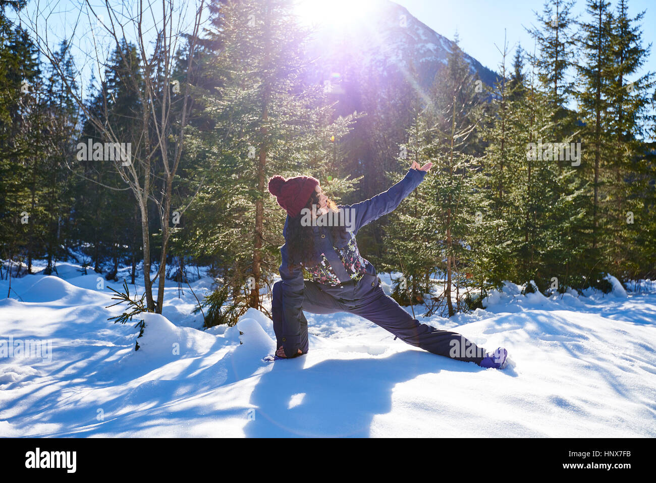 Woman in winter clothes practicing side angle yoga pose in snowy forest, Austria Stock Photo