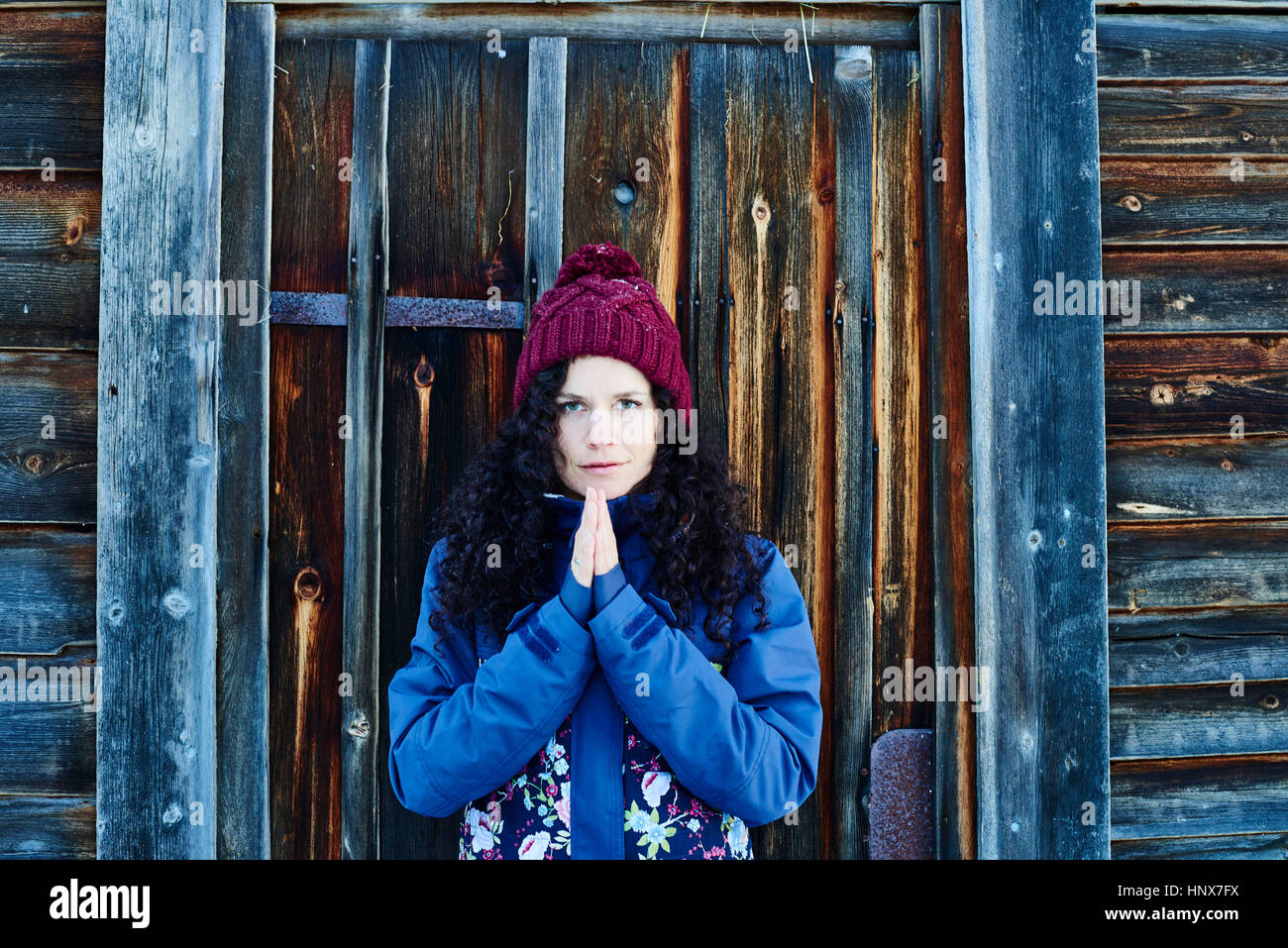Portrait of woman in knit hat practicing yoga, meditating by log cabin door Stock Photo