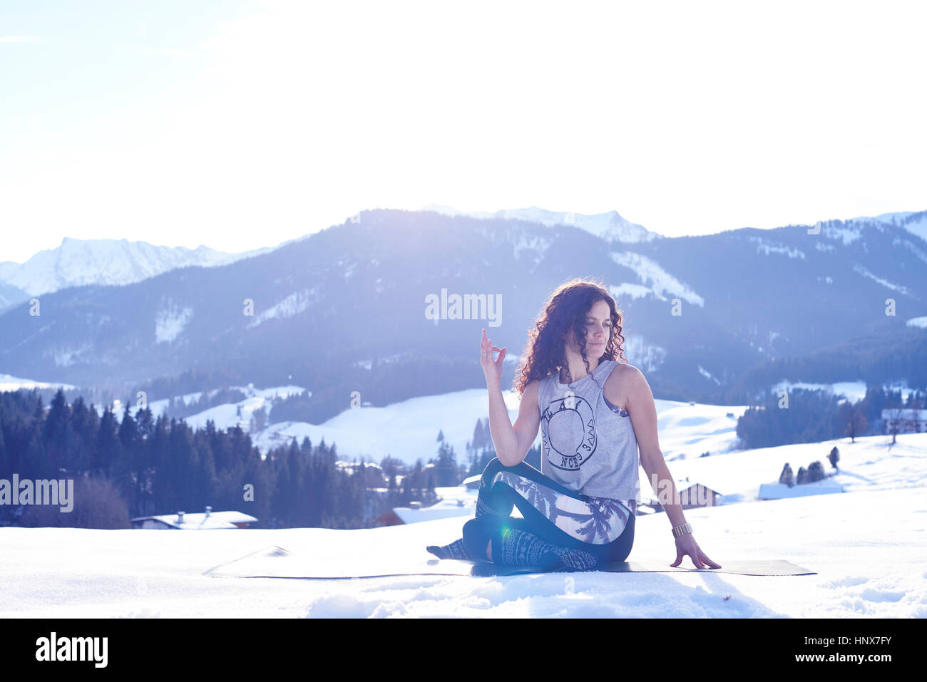 Woman practicing sage yoga pose in snowy sunlit landscape, Austria Stock Photo