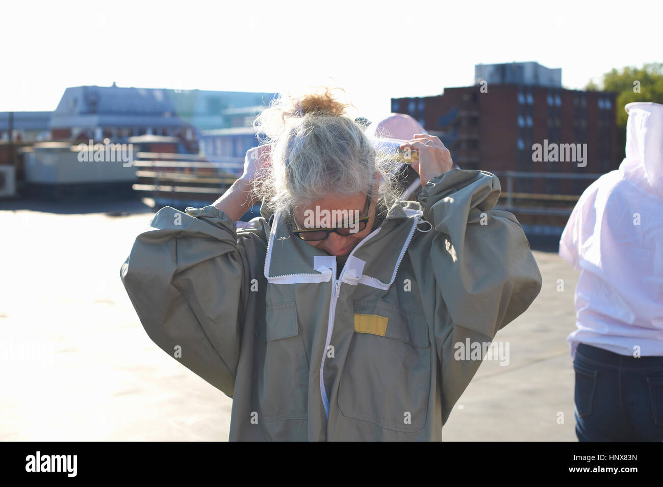 Female beekeeper putting on protective clothes on city rooftop Stock Photo