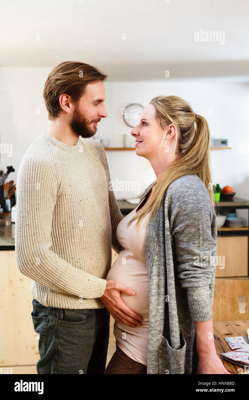 Man touching pregnant girlfriend's stomach in kitchen Stock Photo
